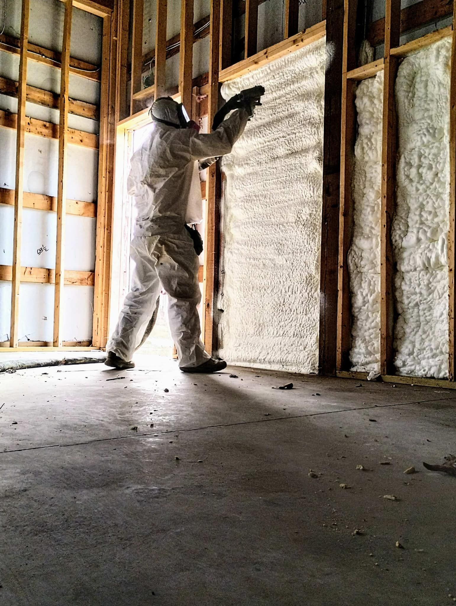 A man in a protective suit is spraying insulation on a wall.