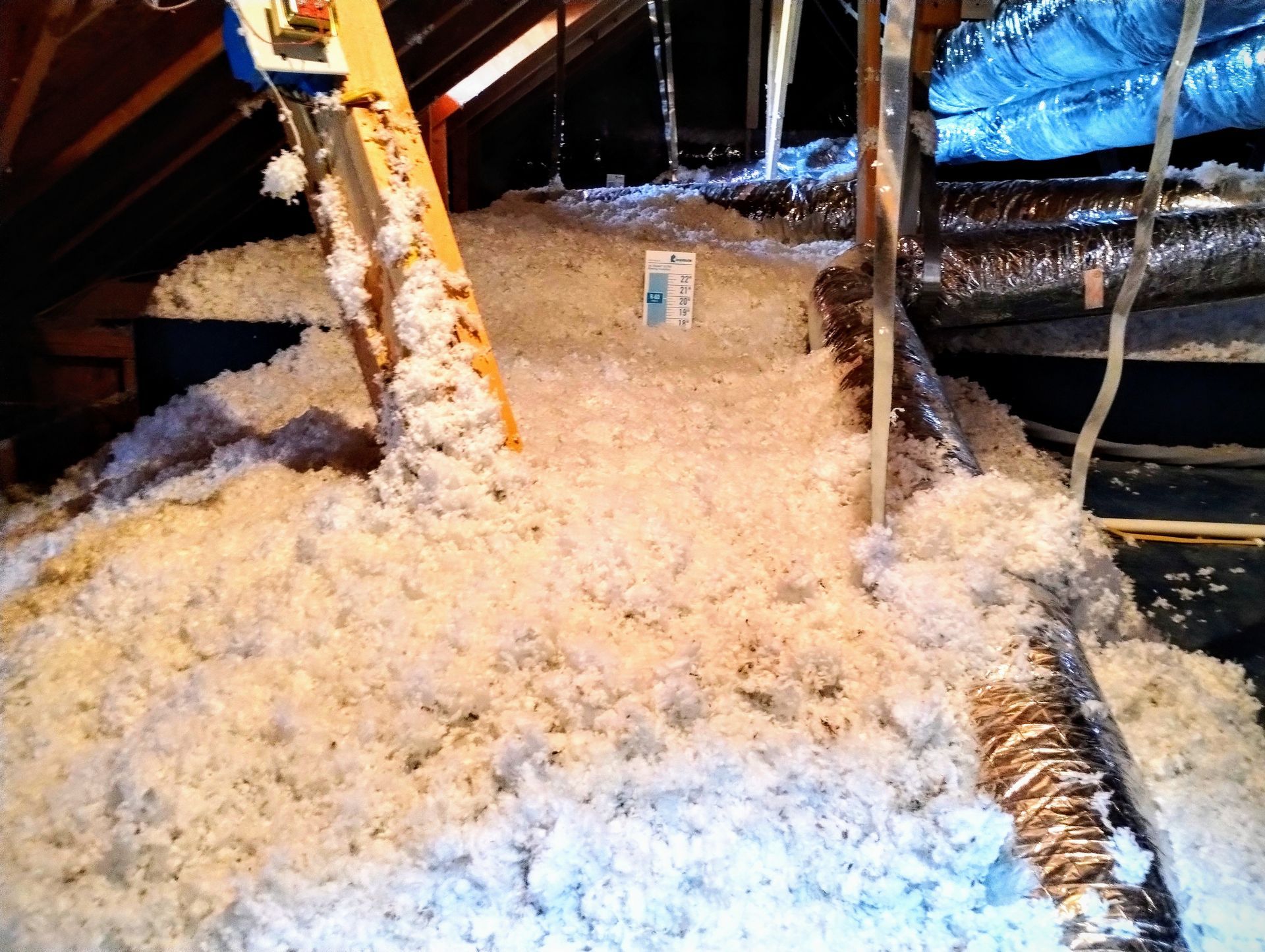 A pile of insulation in an attic with a ladder in the background