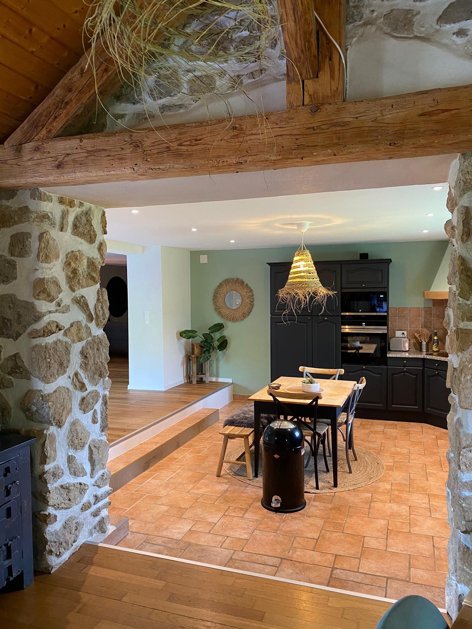 Vue intérieure d'une cuisine rustique avec murs en pierre, poutres en bois et table à manger.