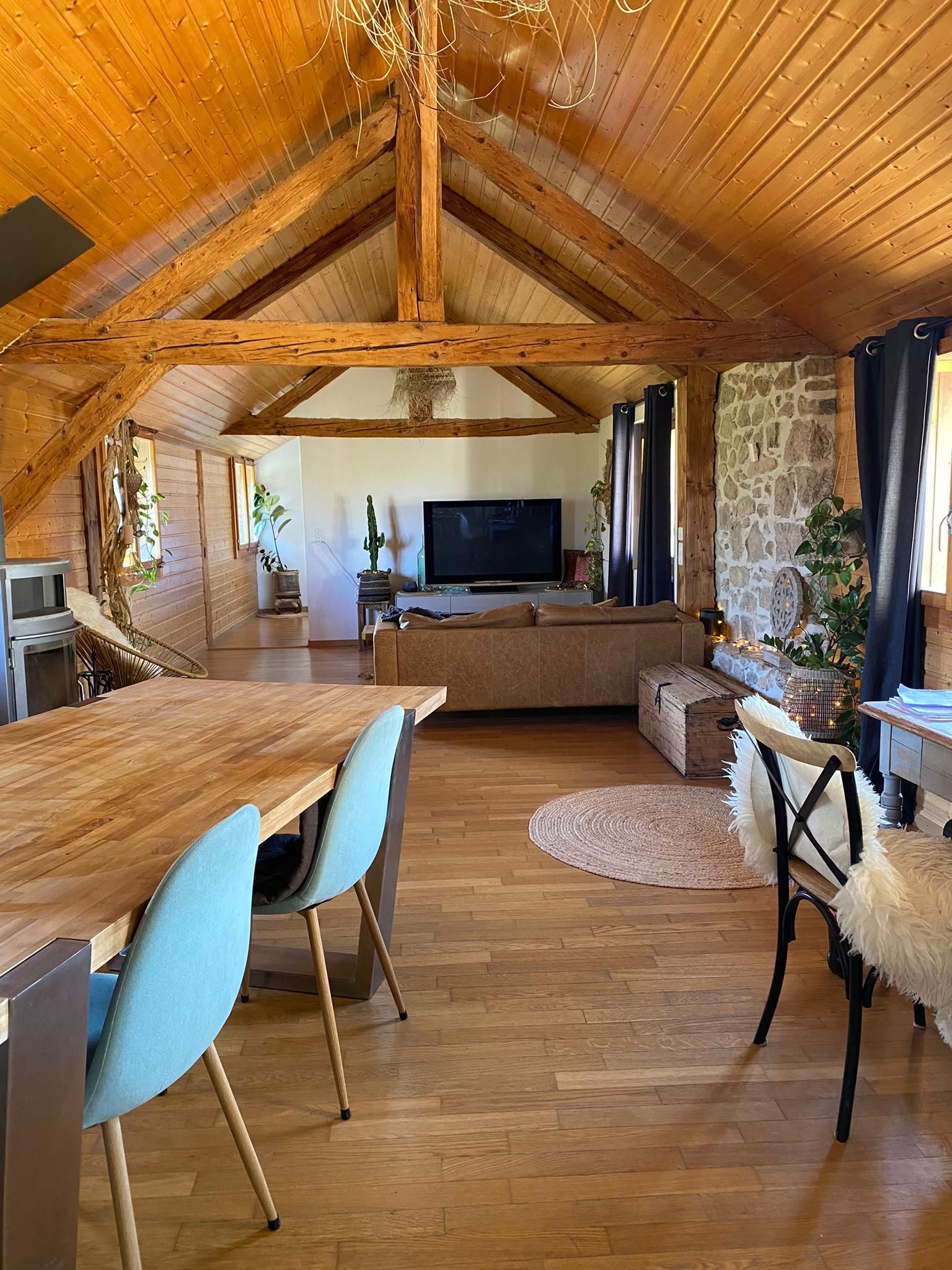 Intérieur d'un espace de vie rustique avec poutres apparentes, parquet, table à manger et canapé avec télévision.
