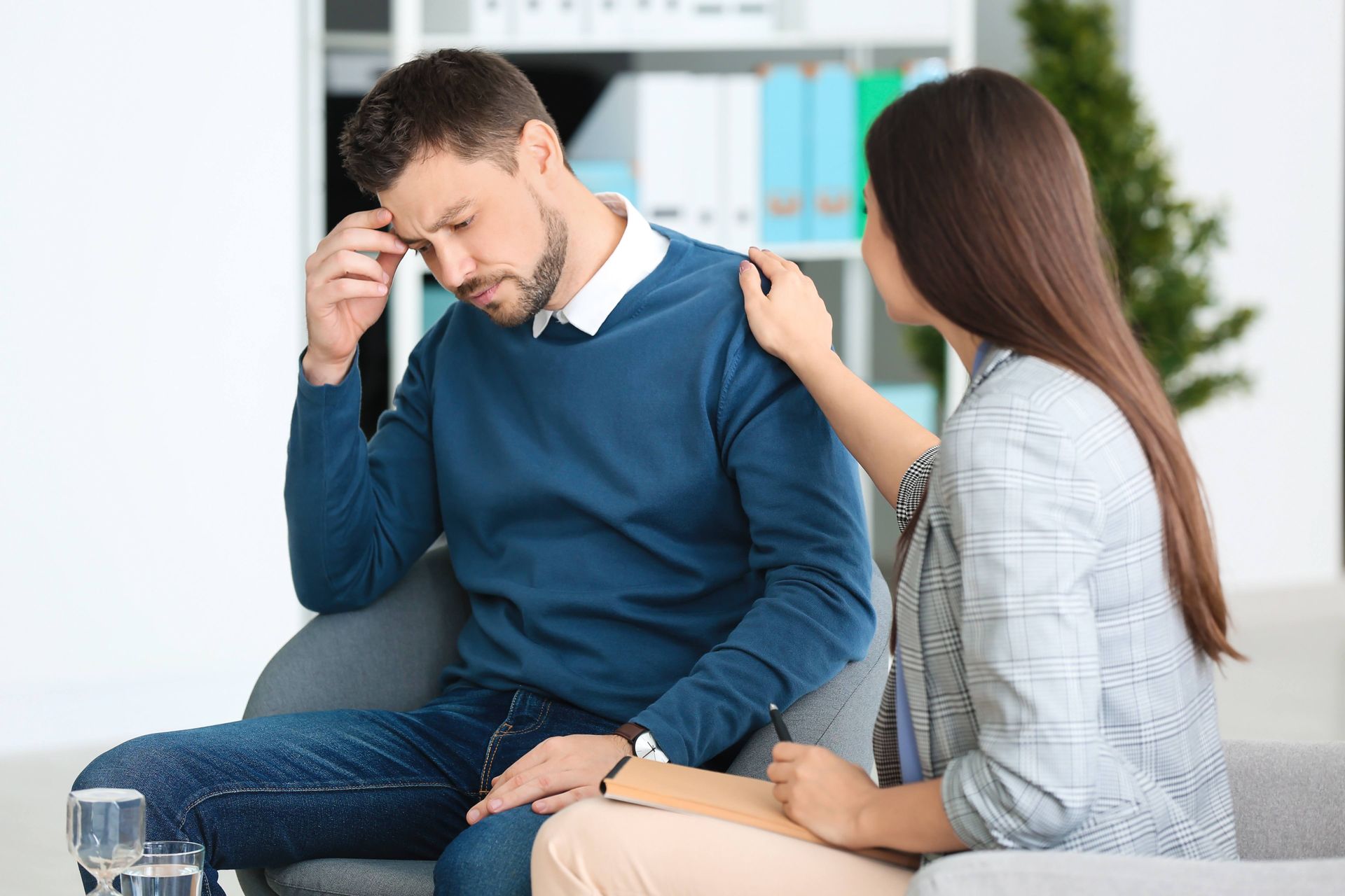 a woman is comforting a man who is sitting on a couch