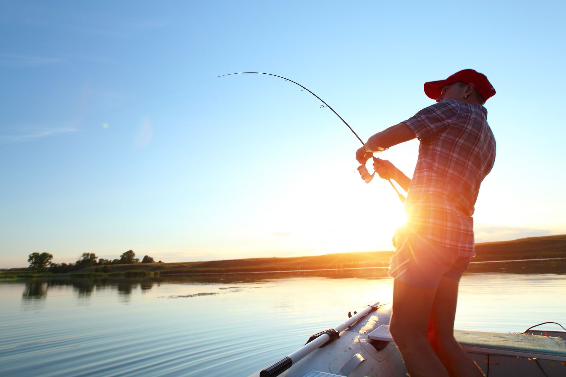 a man is fishing from a boat on a lake at sunset