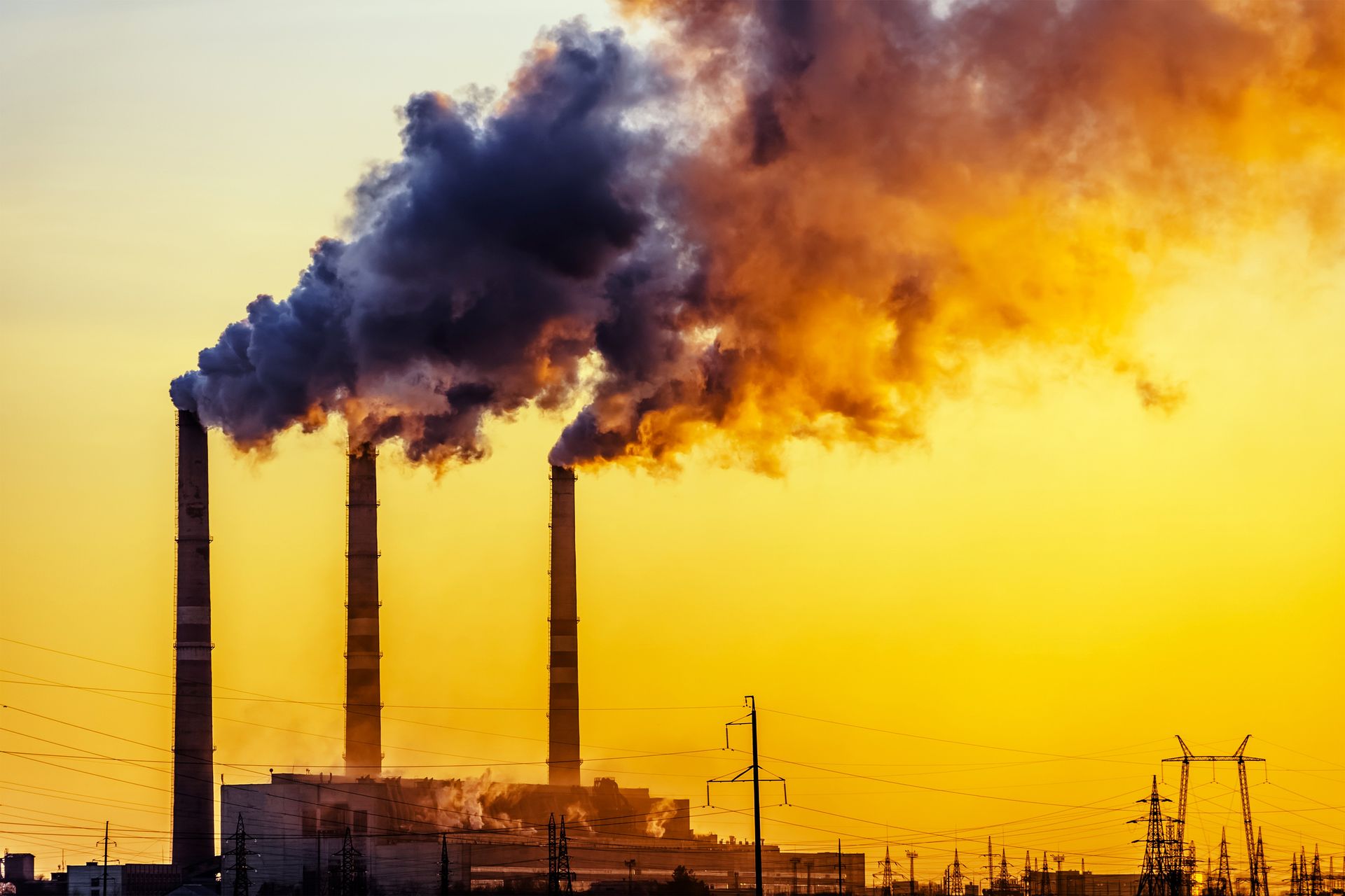 a factory with smoke coming out of the chimneys at sunset