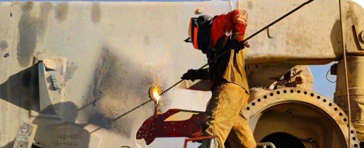 Una persona con equipo de seguridad soldando una gran estructura industrial al aire libre.