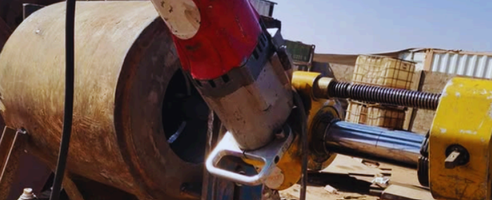 Una herramienta roja y plateada trabajando en un tambor cilíndrico de hormigón en un entorno al aire libre.