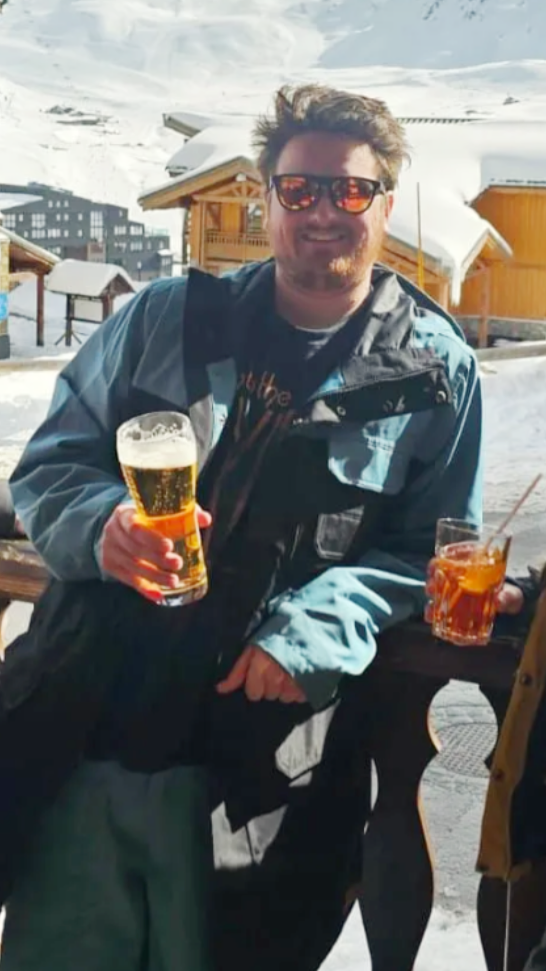 A man is holding a glass of beer in the snow.