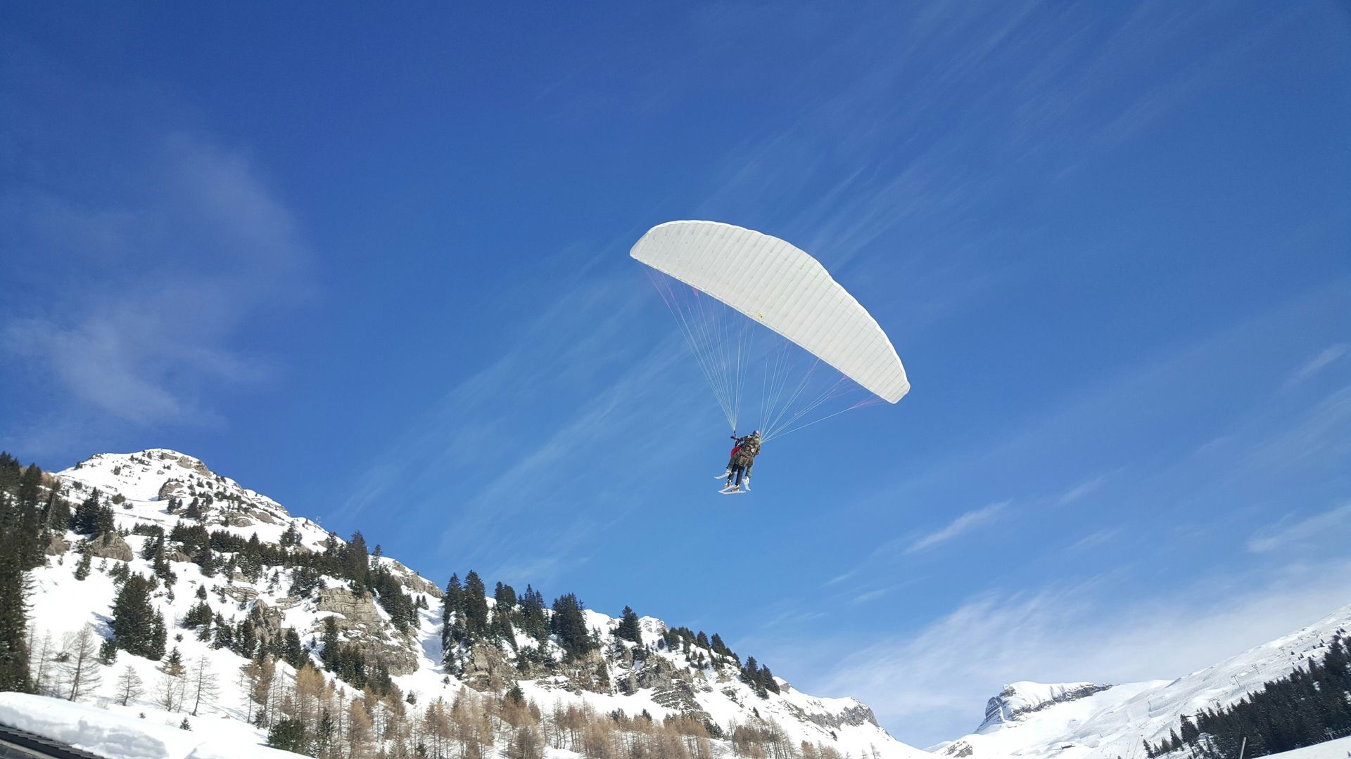 A person is parasailing over a snowy mountain