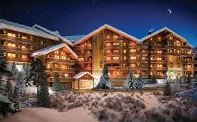 A large building with a lot of windows is surrounded by snow and trees at night.