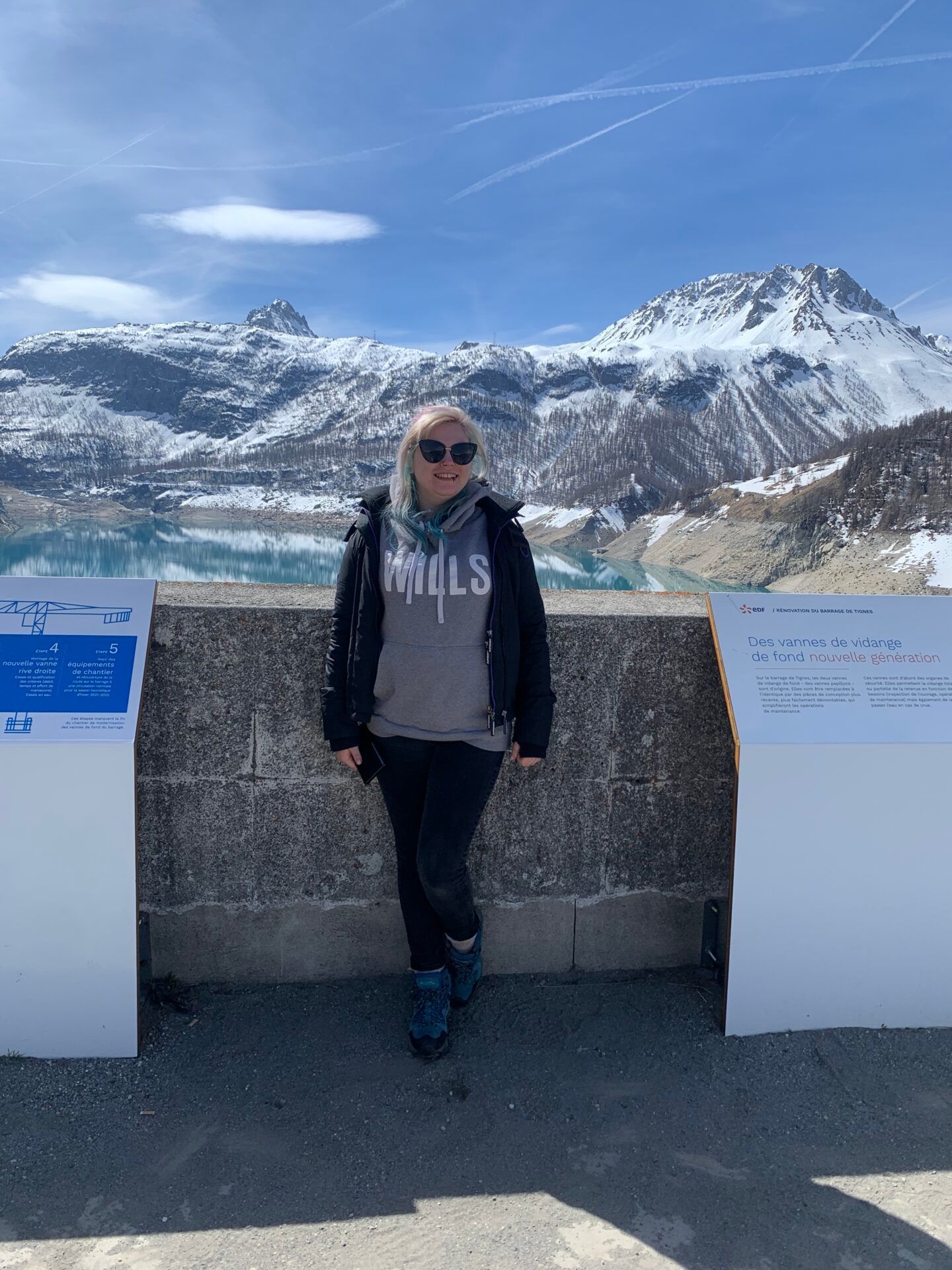 A woman is standing next to a wall with a mountain in the background.
