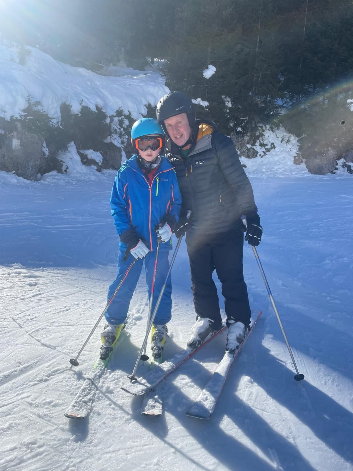 A man in skiing gear on skis with his child, surrounded by snow