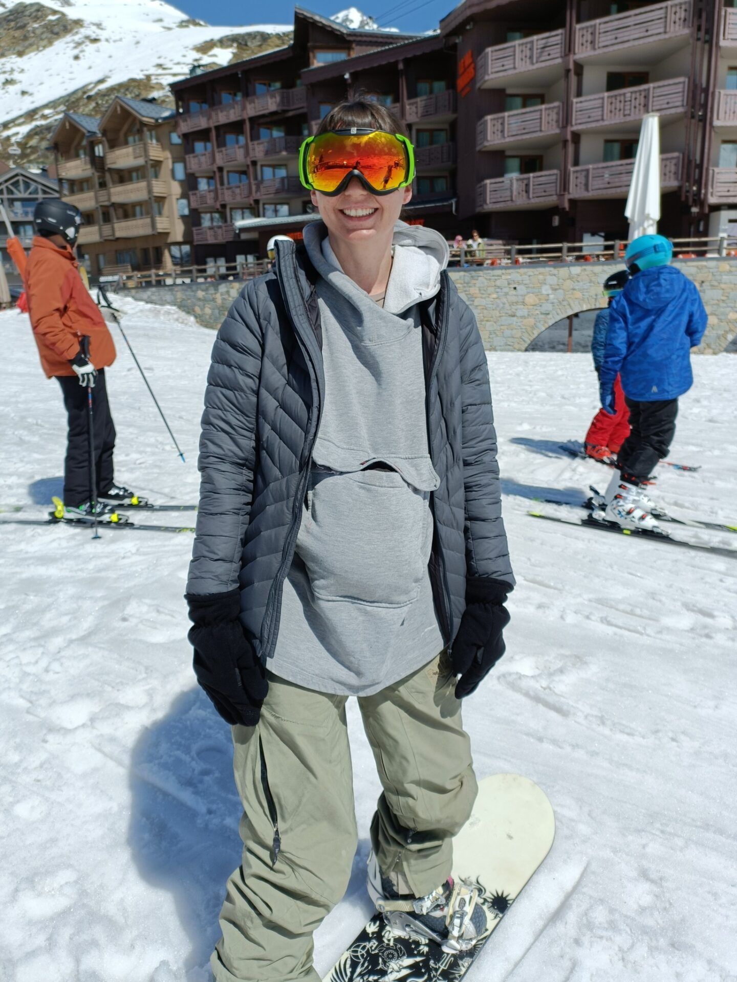 A woman wearing goggles is standing on a snowboard in the snow.