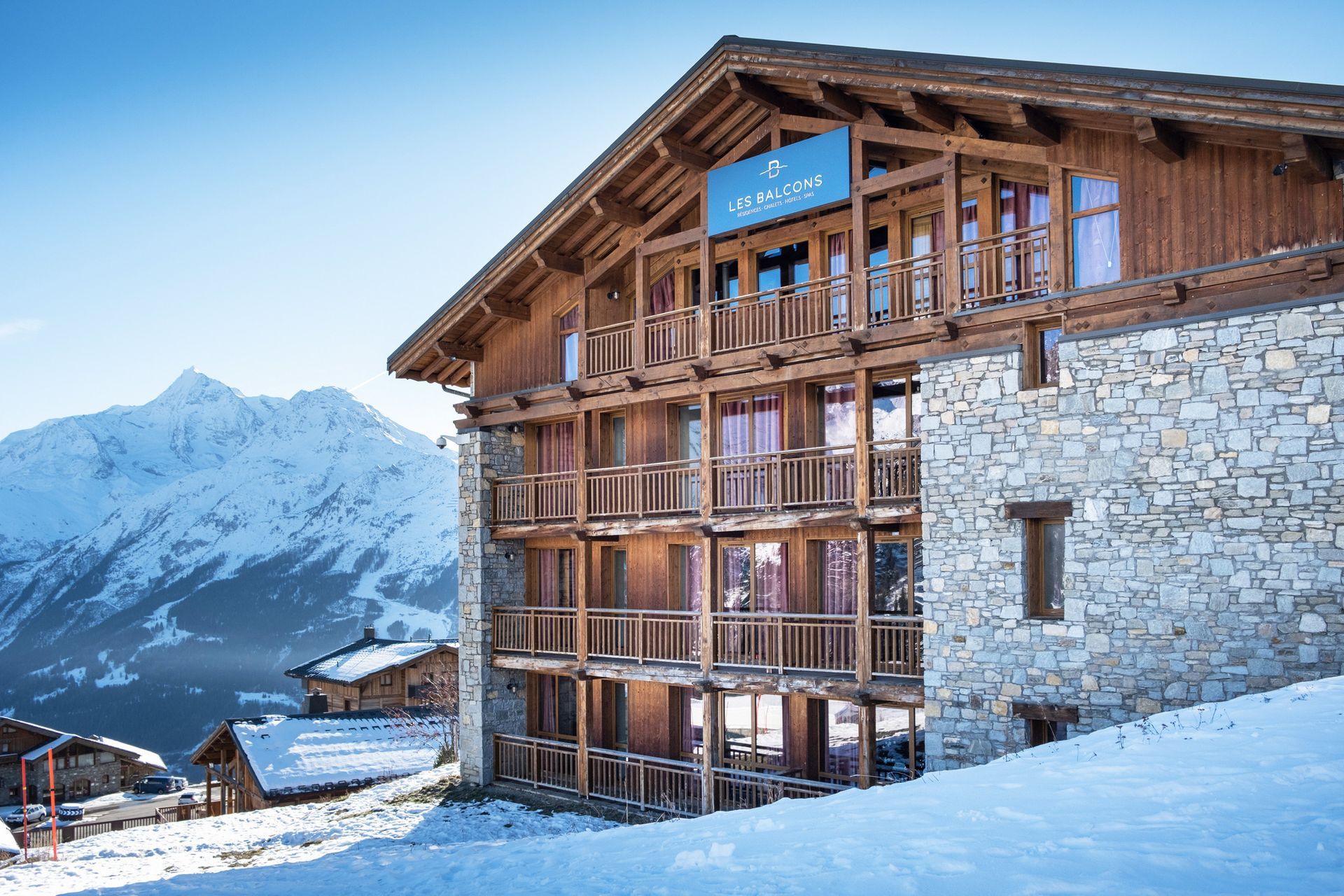 An image of Les Balcons de la Rosiere which is a large stone building is sitting on top of a snow covered hill.