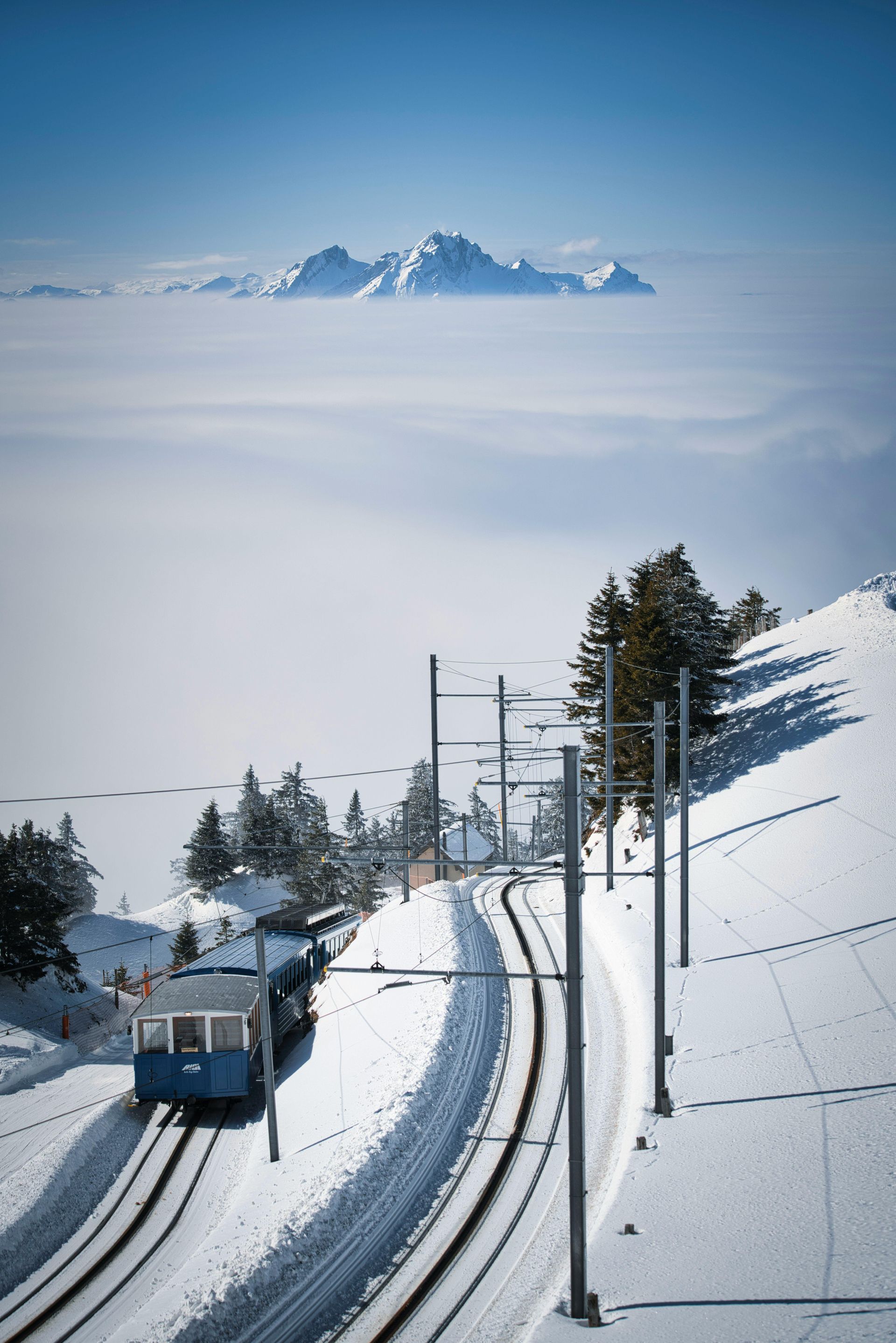 A train is going down the tracks in the snow with mountains in the background