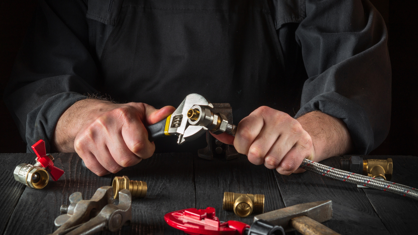 a man is sitting at a table working on a pipe with a wrench .