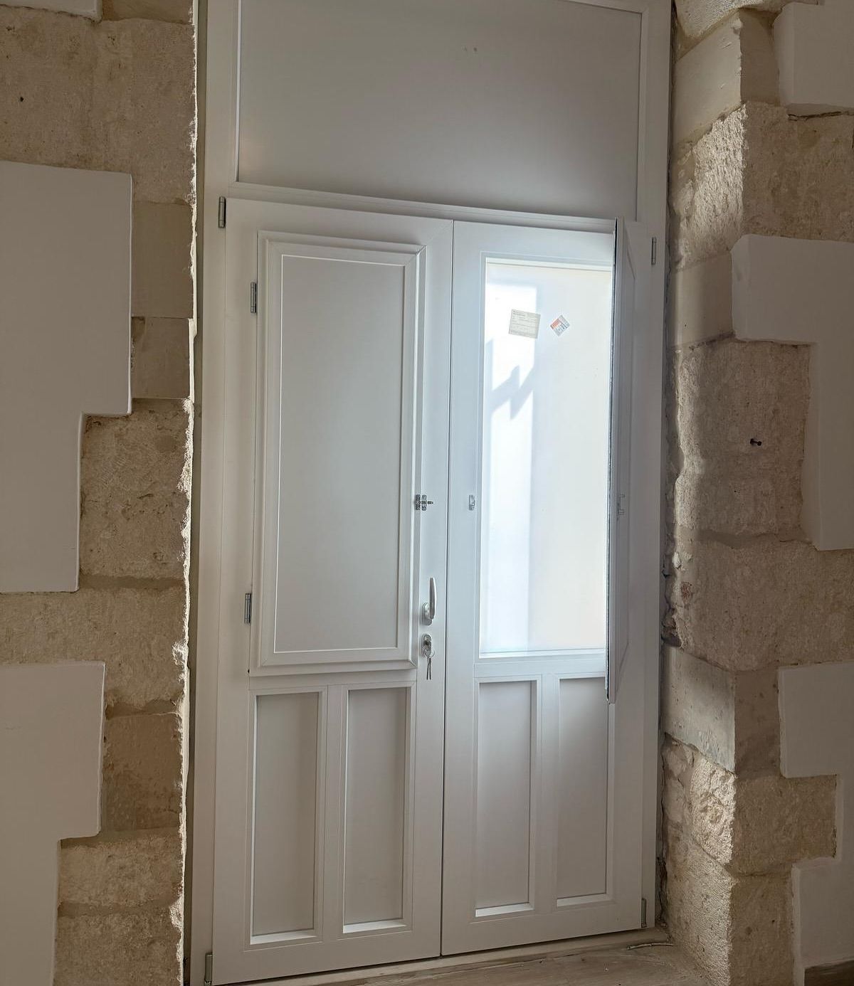 Una porta bianca con una finestra tra due muri di mattoni