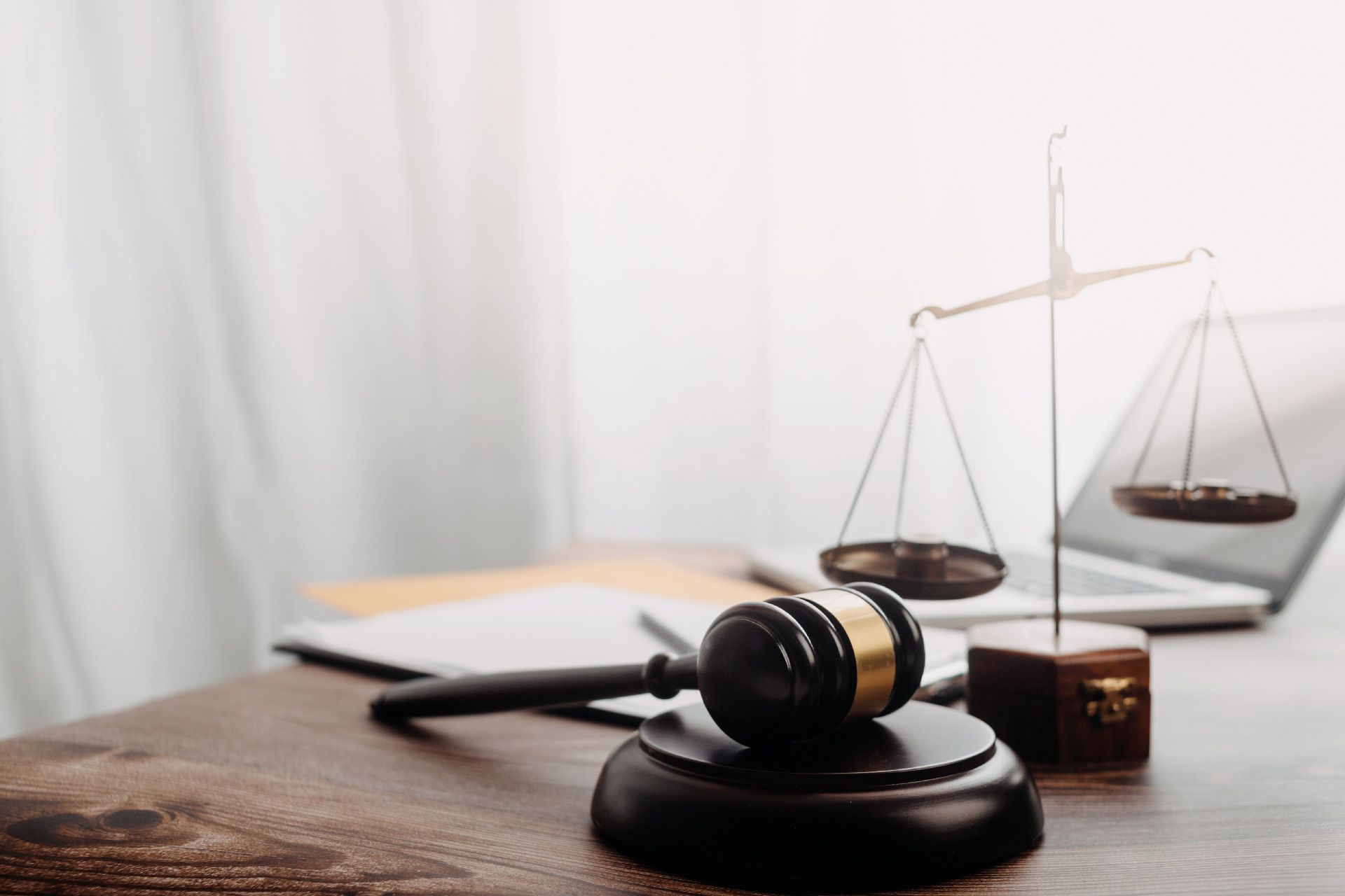 Mazo y balanza sobre un escritorio de madera, símbolo de justicia. Al fondo, una computadora portátil.