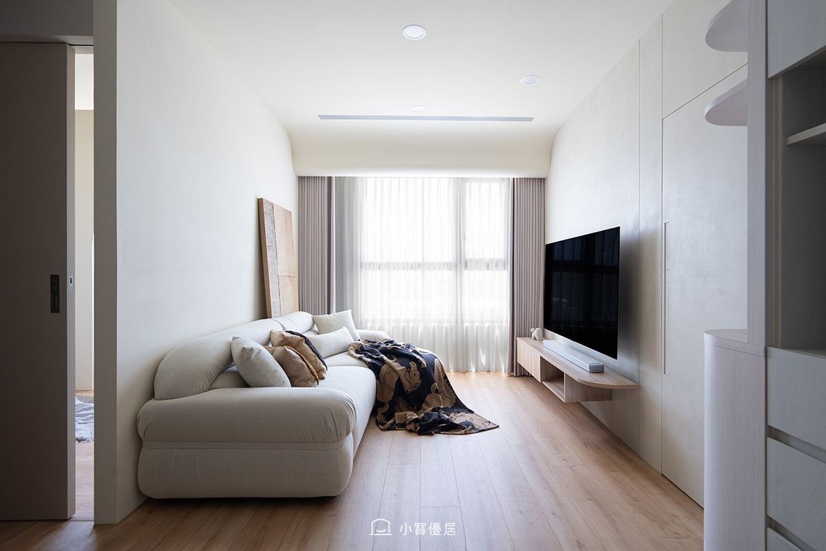 Cozy living room: beige sofa, textured wall art, neutral tones, wooden floor, and a blanket.