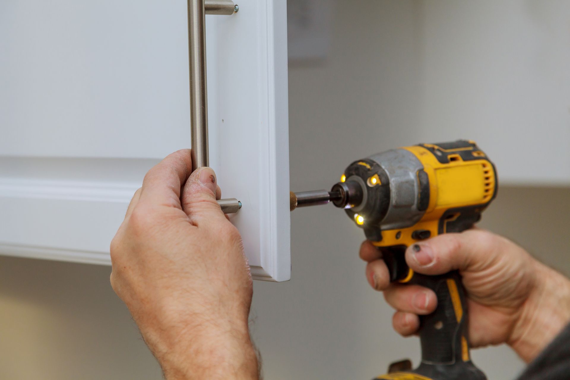 A man is using a drill to install a handle on a cabinet.