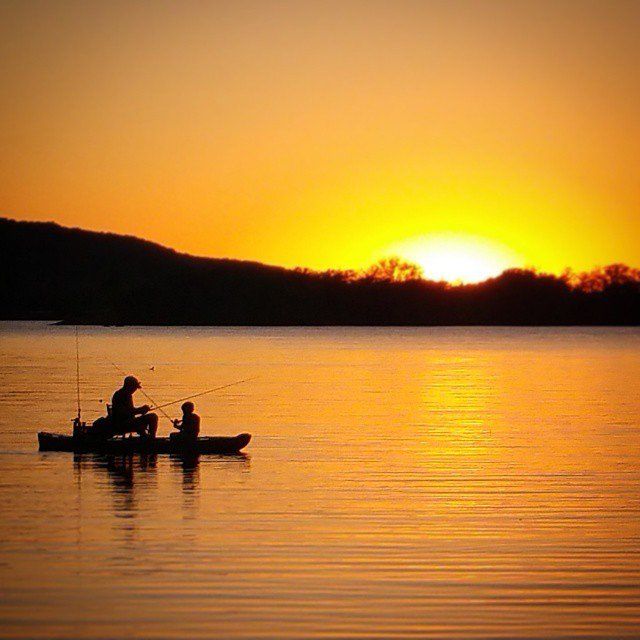 Two people are fishing in a boat on a lake at sunset