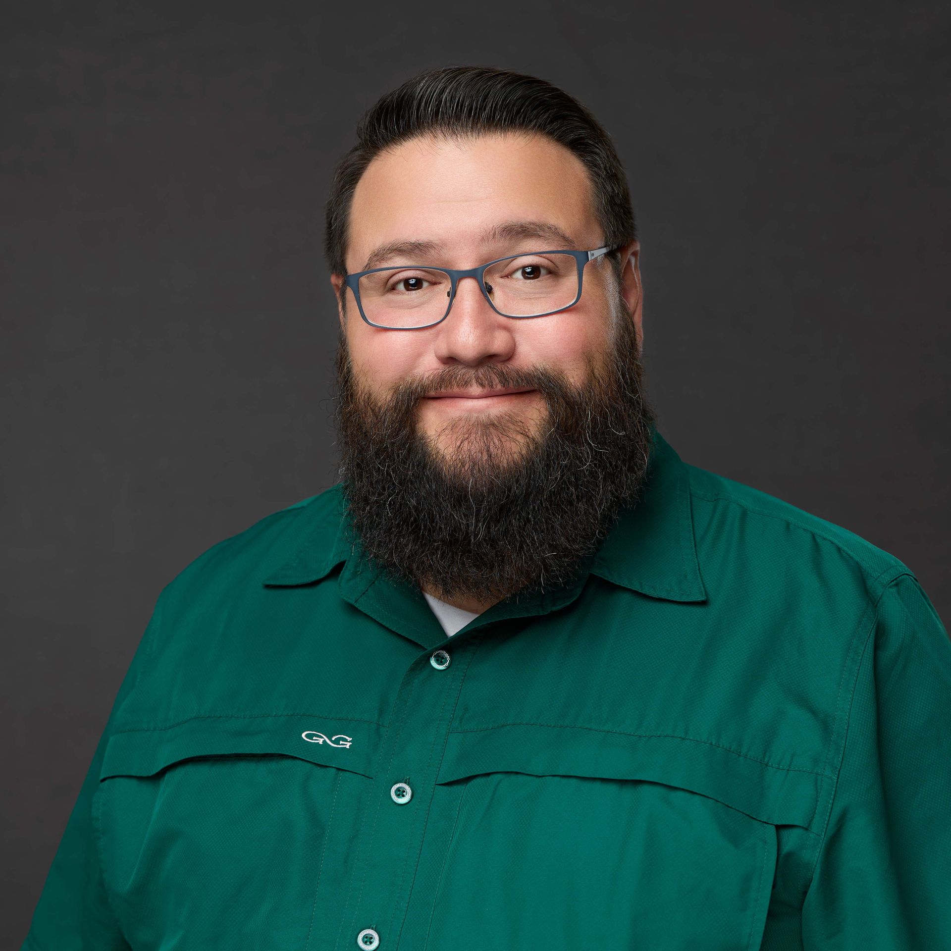 A man with a beard and glasses is wearing a green shirt.