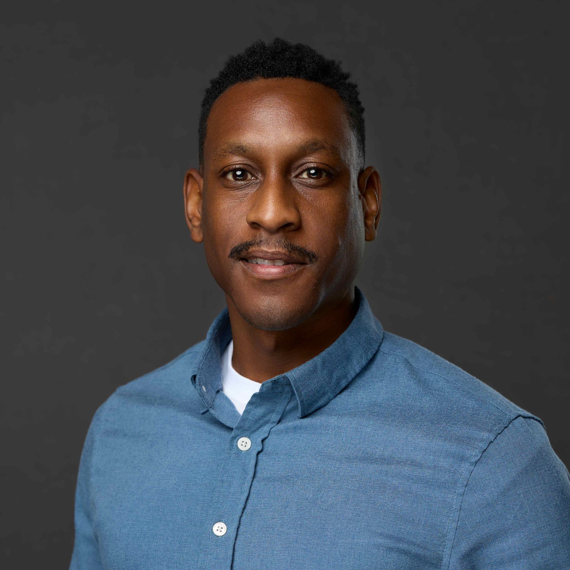 Professional headshot of a man on a solid, dark background