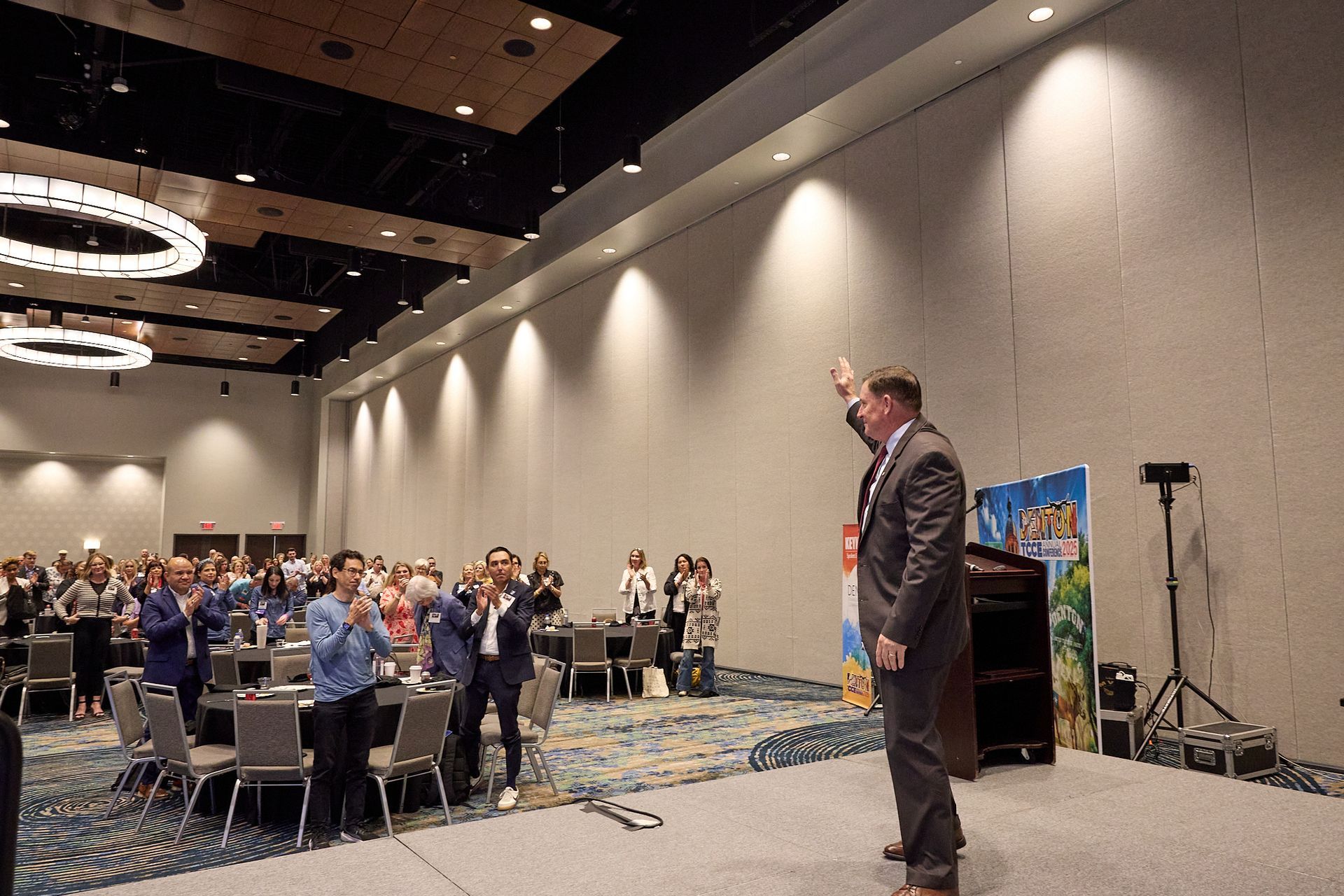 A man in a suit is standing on a stage in front of a crowd of people.
