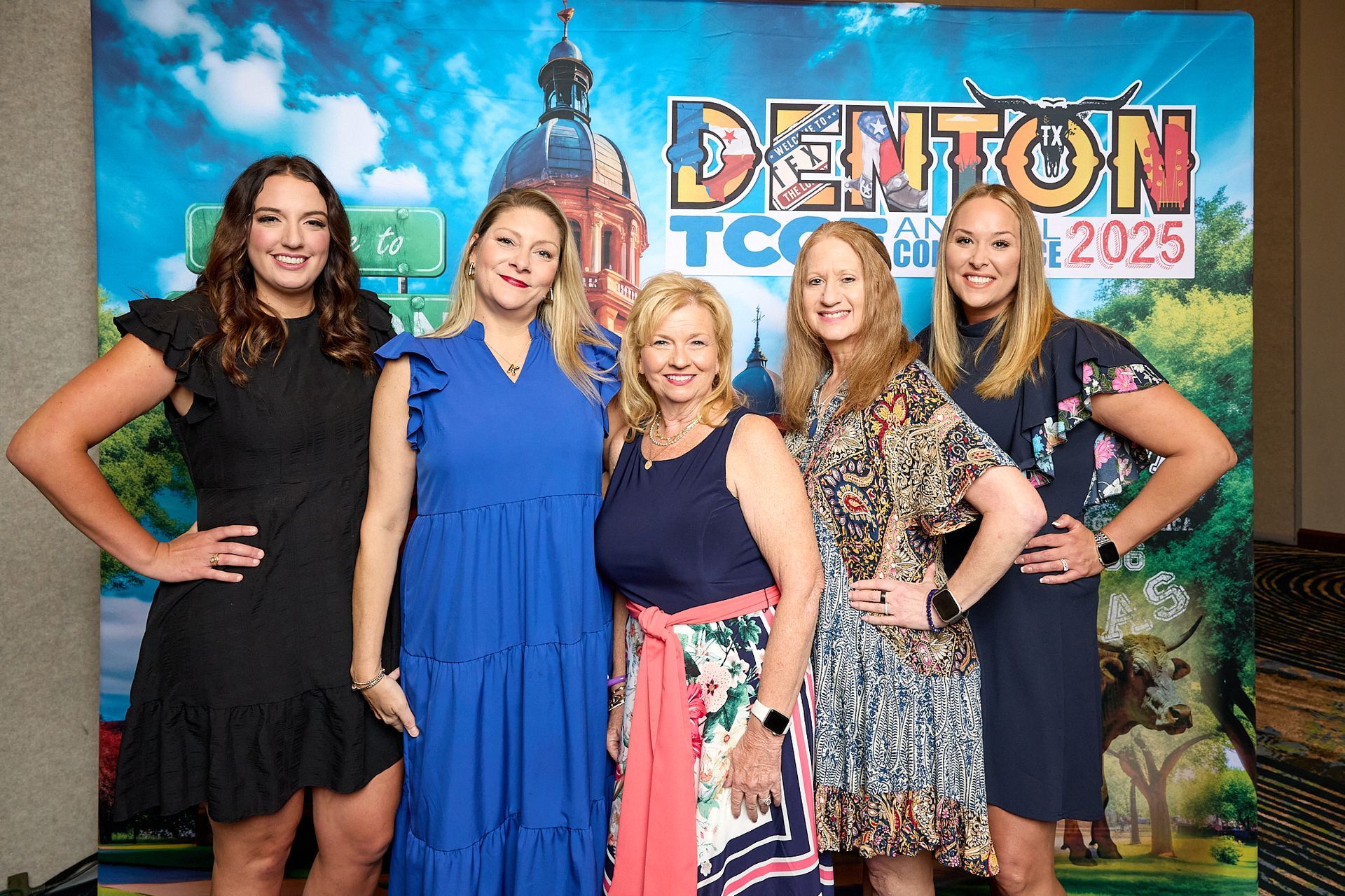 A group of women are posing for a picture in front of a sign that says denton tc.