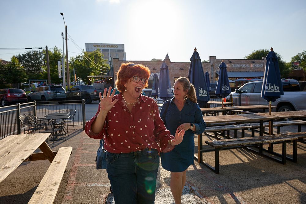 Two women are walking down a sidewalk next to a picnic table.