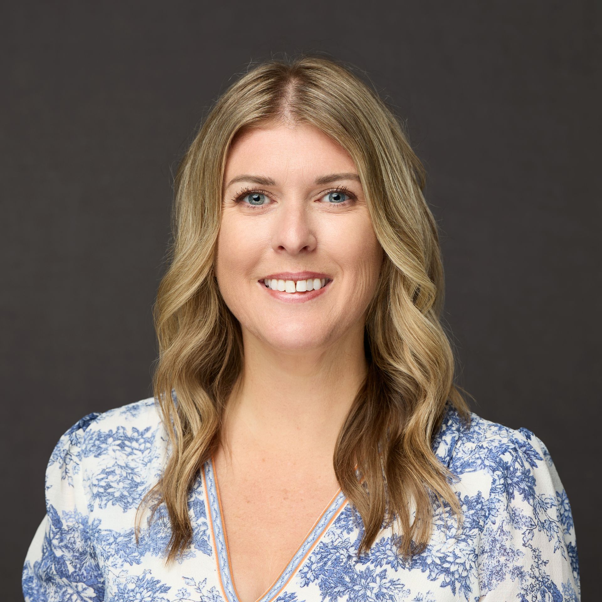 A woman in a blue and white floral shirt is smiling for the camera.