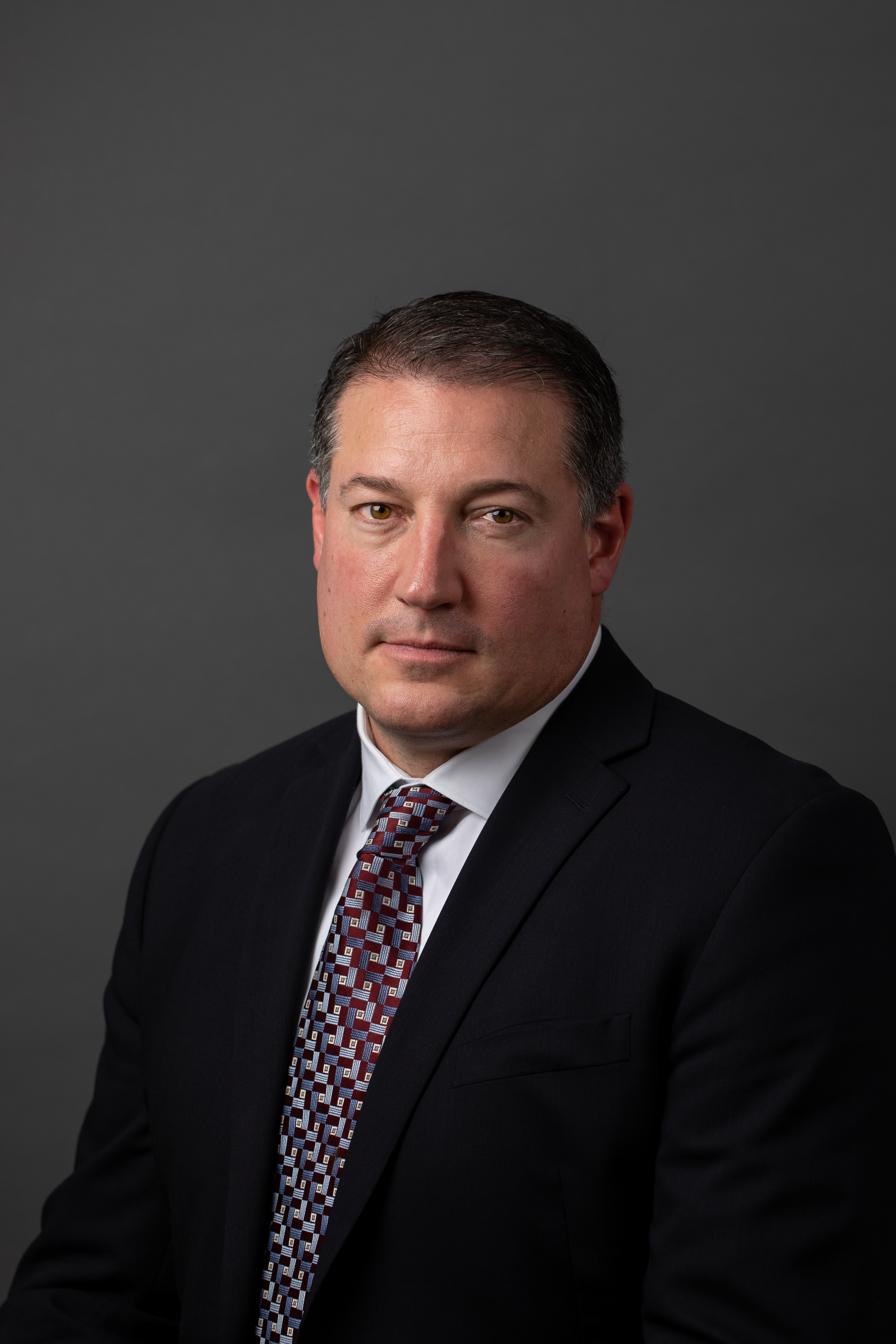 A man in a suit and tie is standing in front of a gray background.