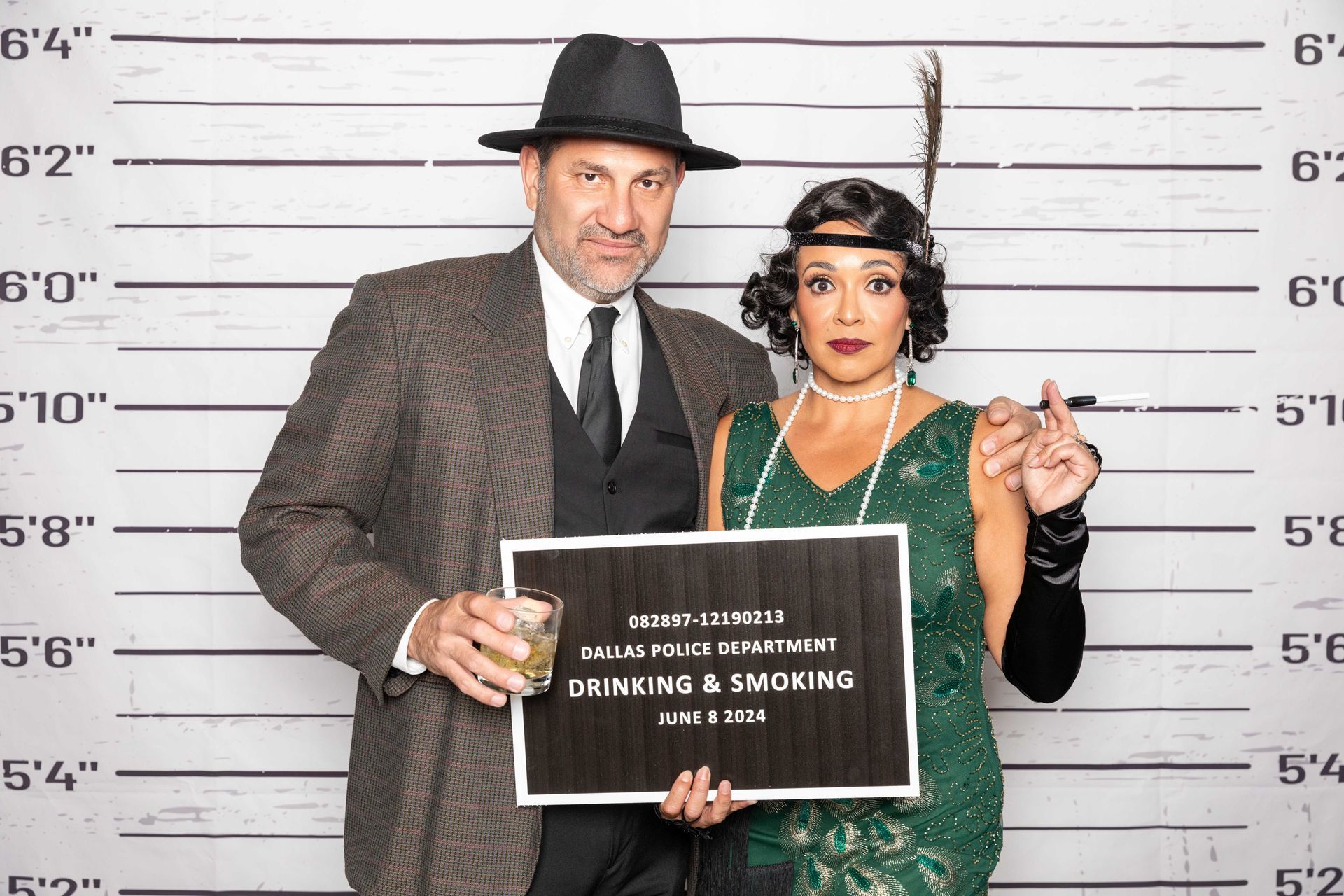 A man and a woman are posing for a picture in front of a police lineup at a party while holding a funny sign.