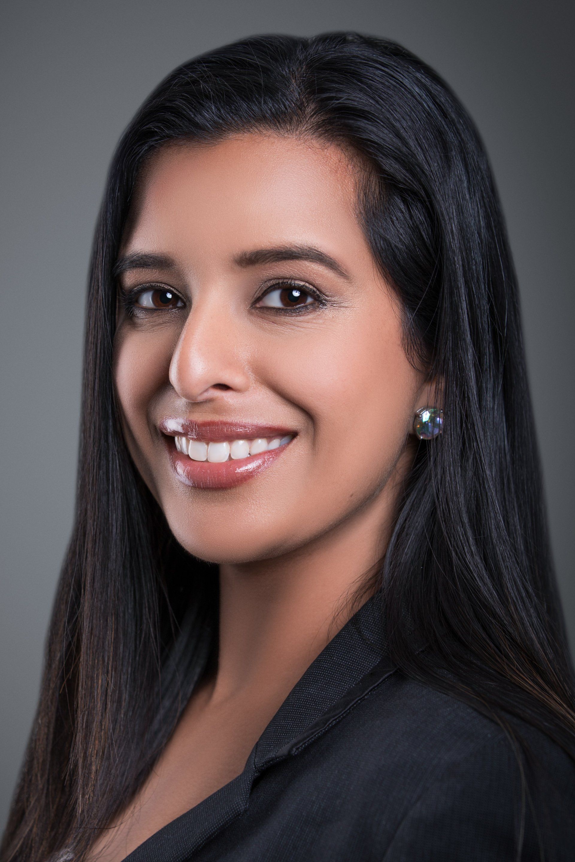 A woman with long black hair and earrings is smiling for the camera.