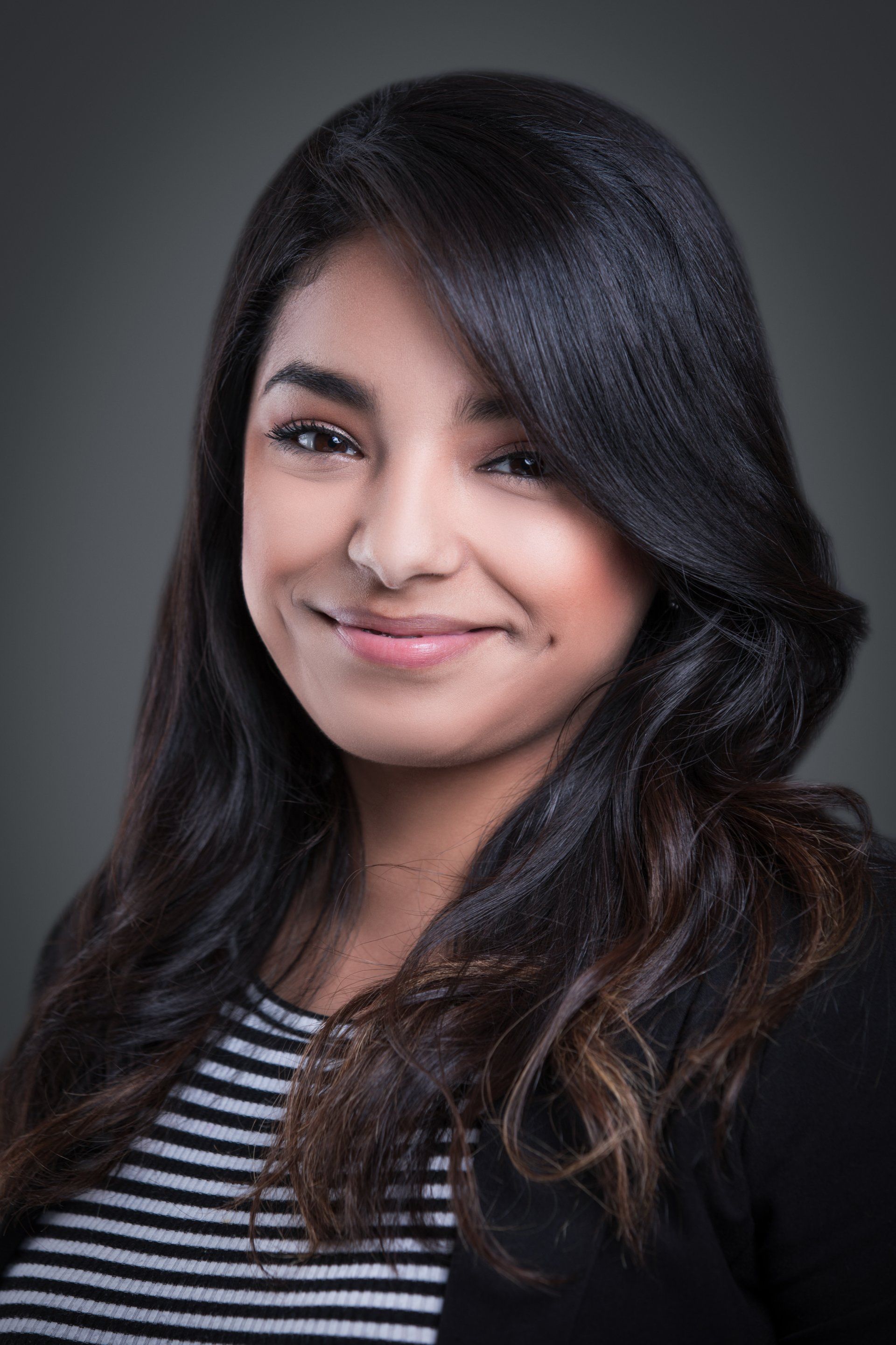 A woman with long hair is smiling for the camera while wearing a striped shirt and a black jacket.