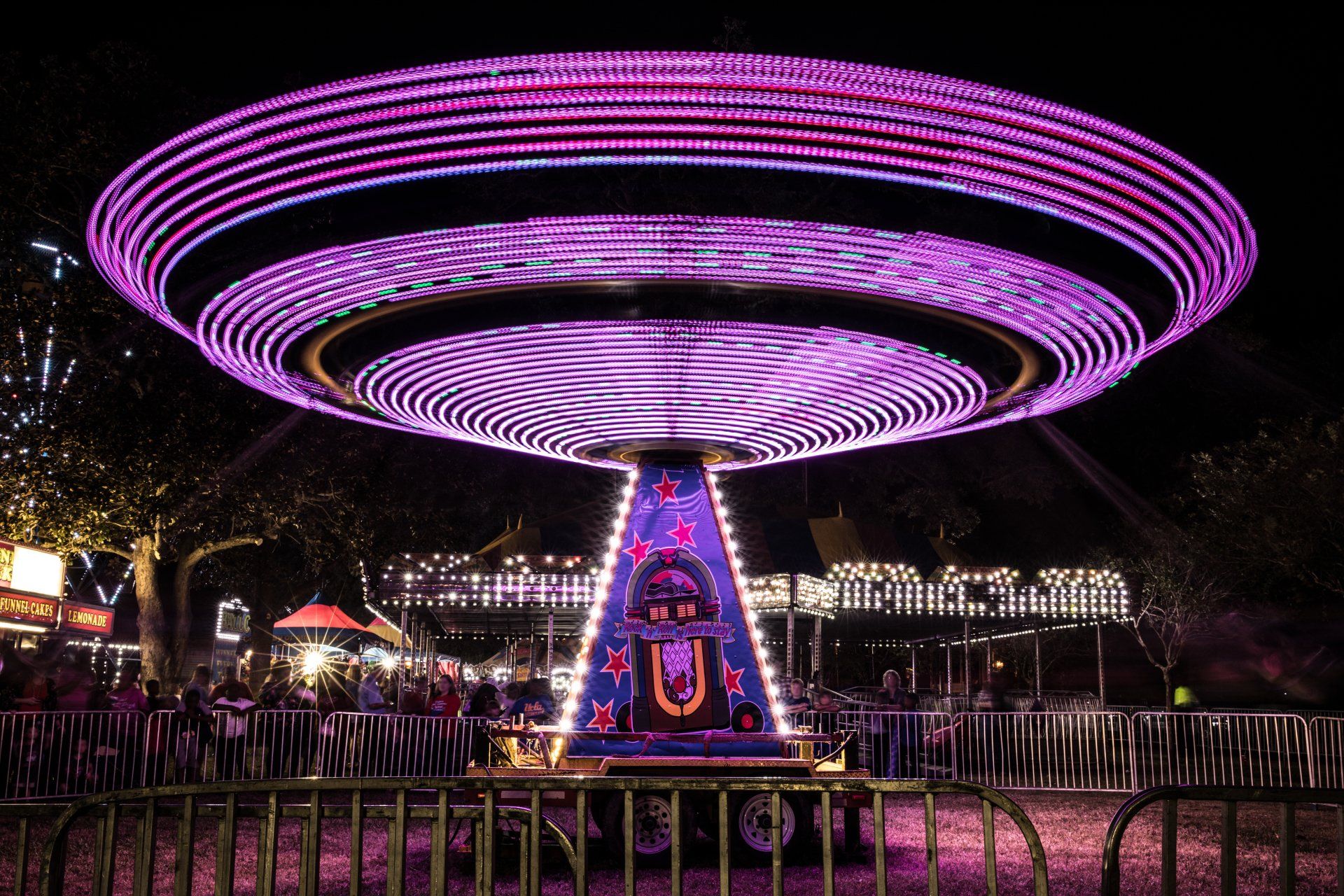 A carnival ride is lit up at night with purple lights.