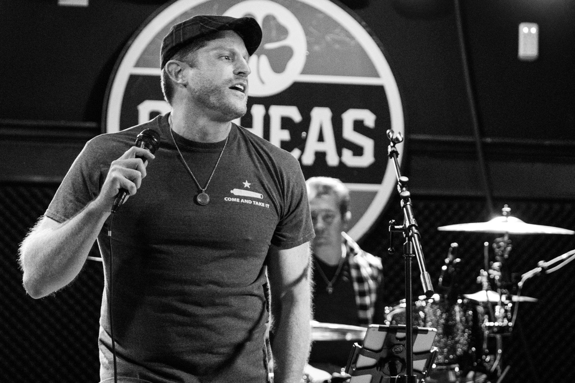 A man is singing into a microphone in front of a sign that says ideas