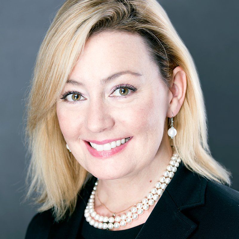 A woman wearing a pearl necklace and earrings is smiling for the camera.