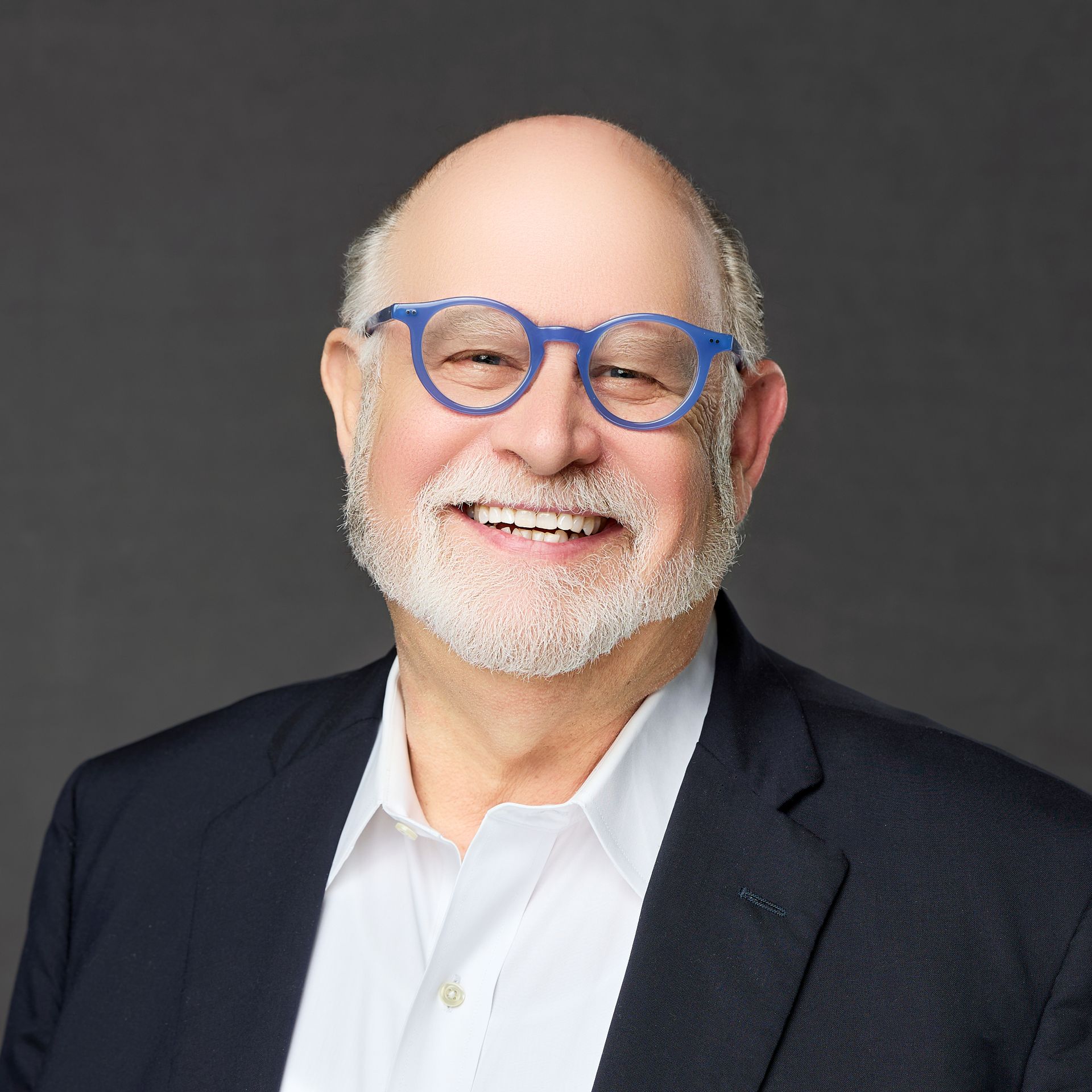 A man with a beard and glasses is wearing a suit and smiling.