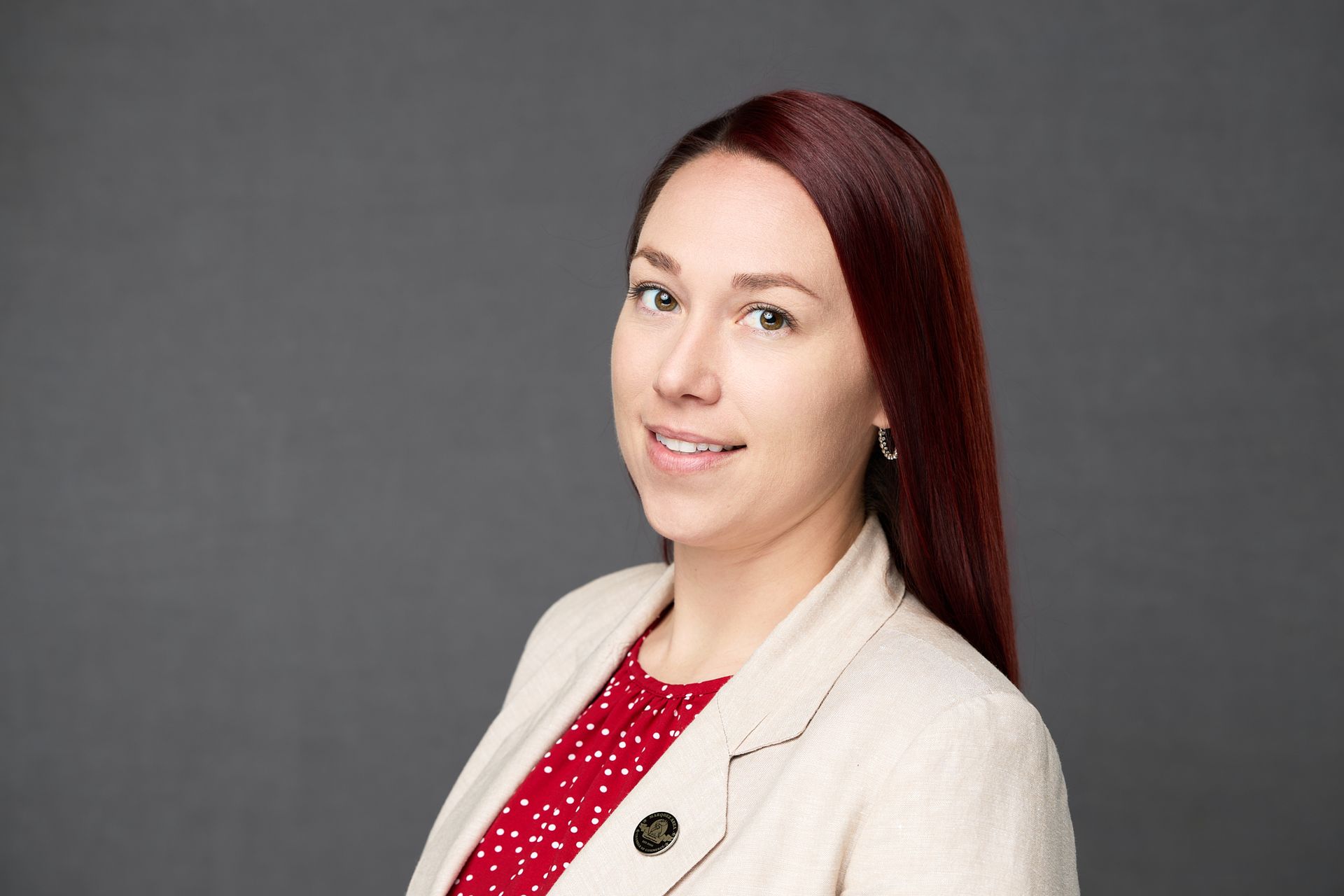 A woman with red hair is wearing a white jacket and a red polka dot shirt while posing for the camera.