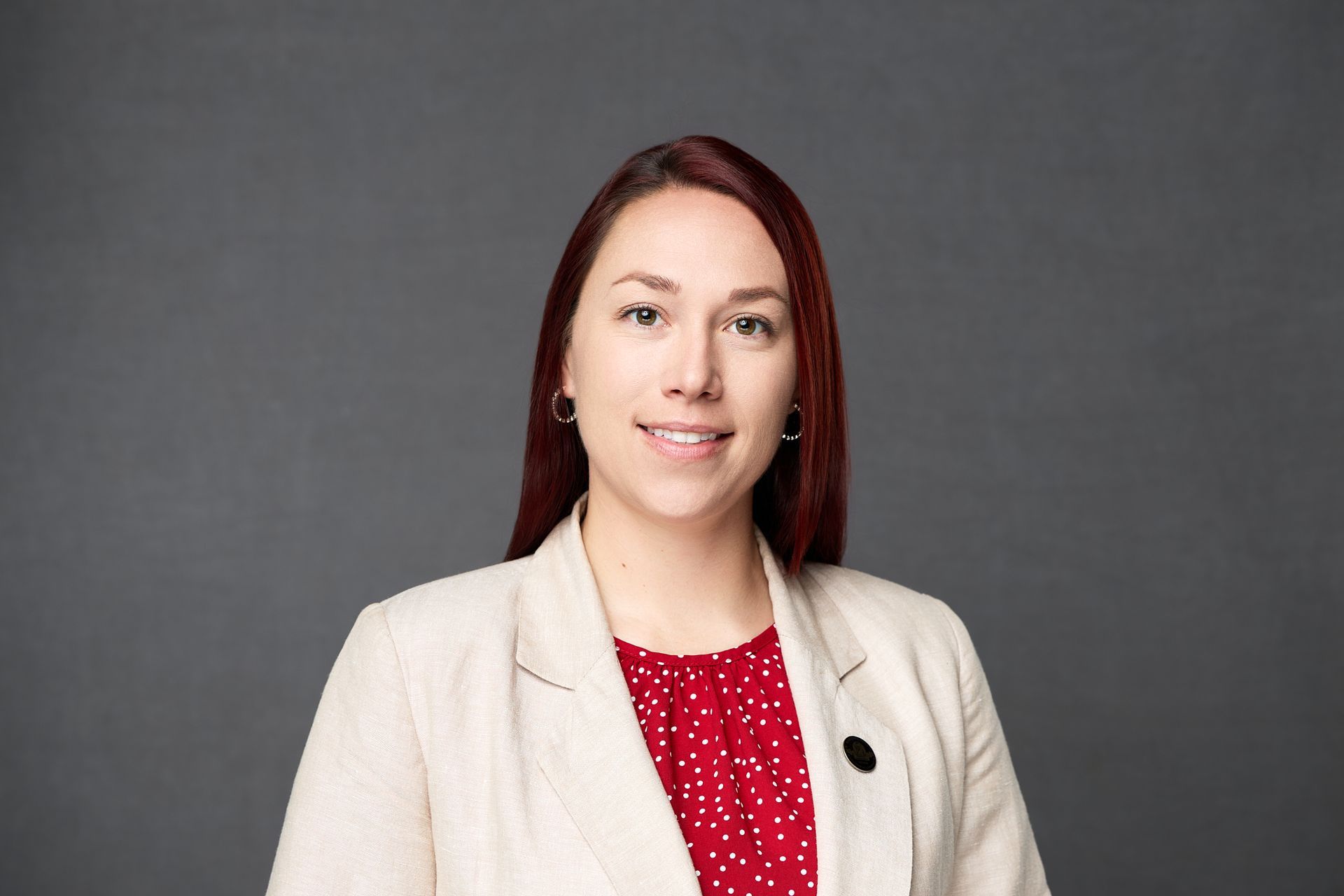 A woman with red hair is wearing a white jacket and a red polka dot shirt while posing for the camera.