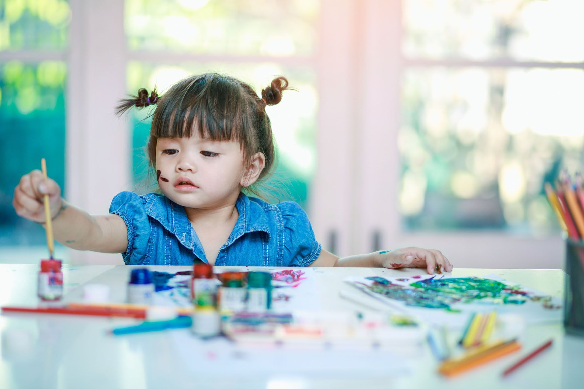 Little girl holding a paint brush — Ames, IA — Ames Community Preschool Center (ACPC)