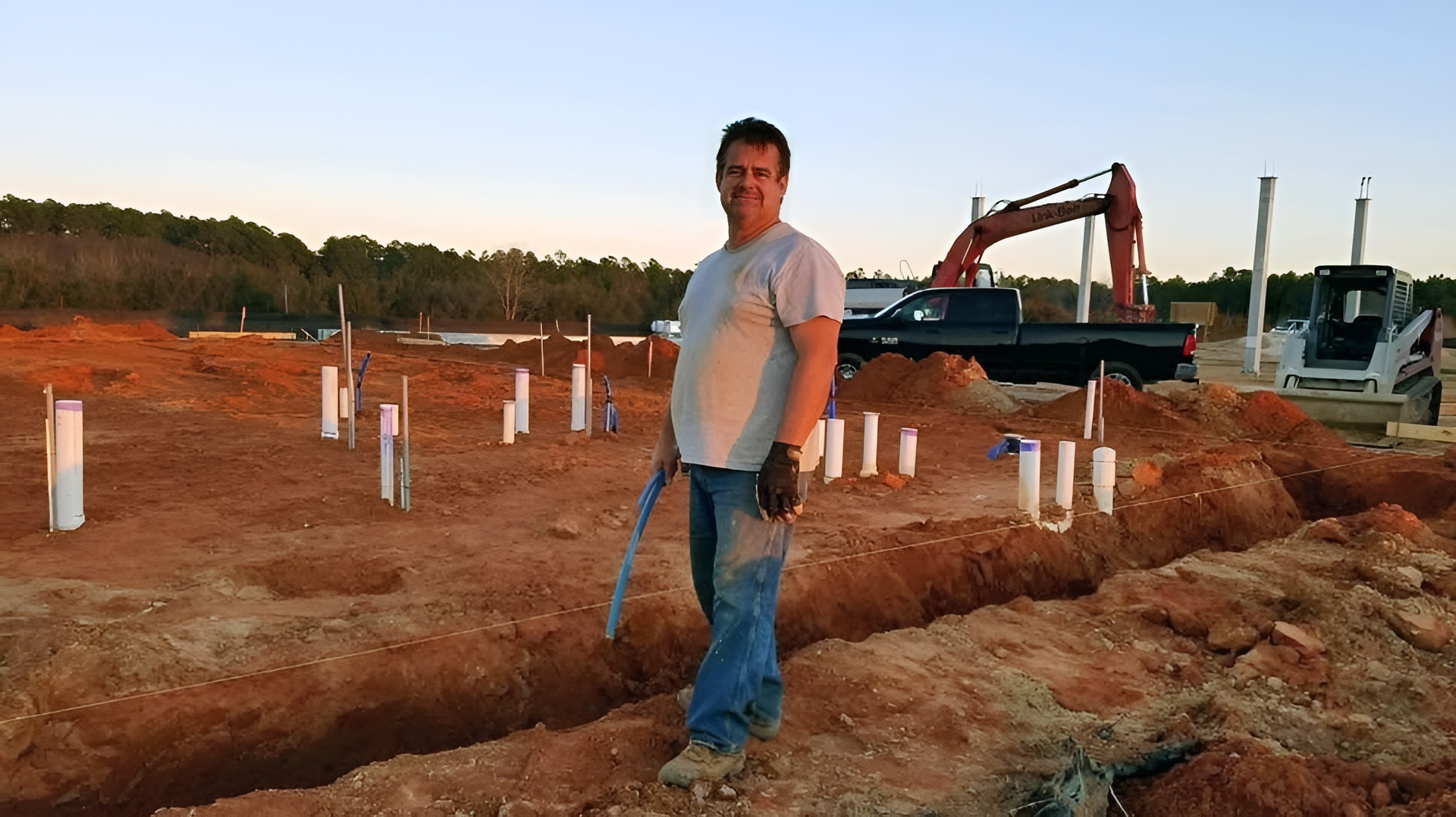 A man in a white shirt is standing in a dirt field