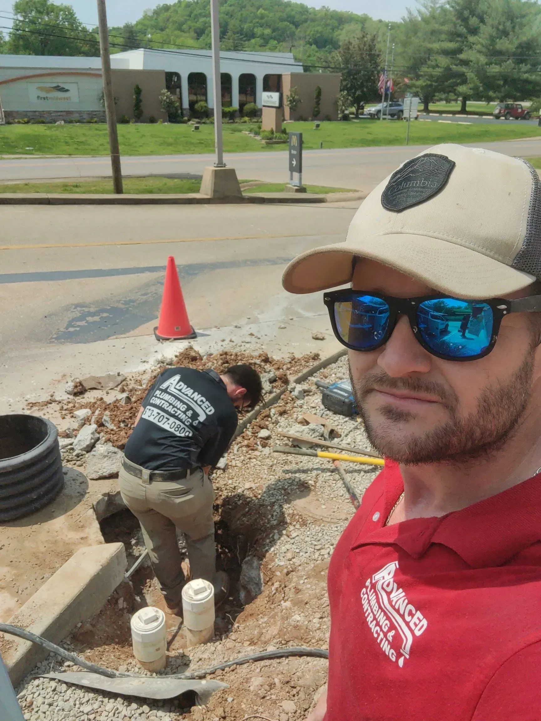 A man wearing sunglasses and a hat is standing in front of a construction site.