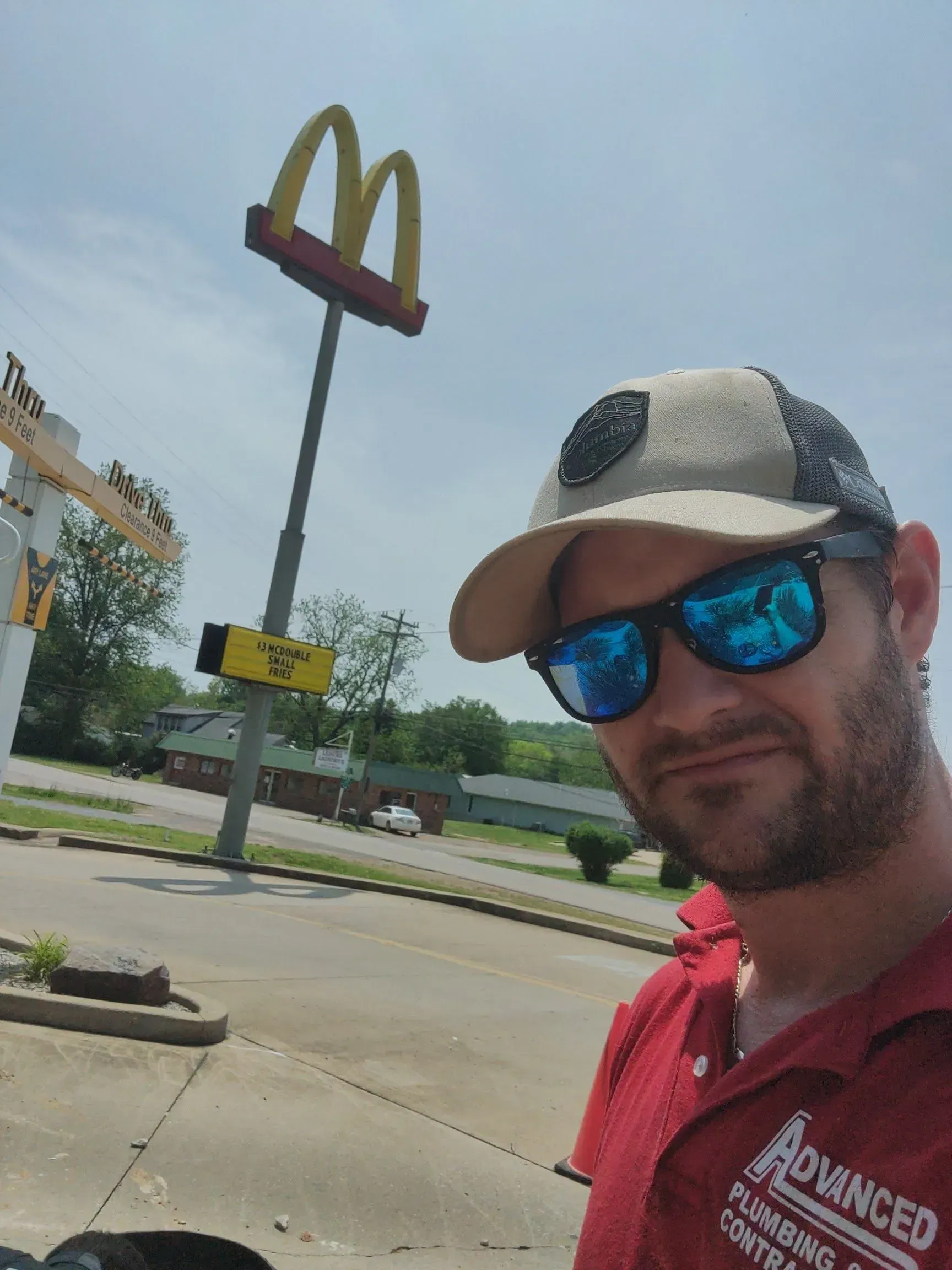 A man wearing sunglasses and a hat is standing in front of a mcdonald 's sign.