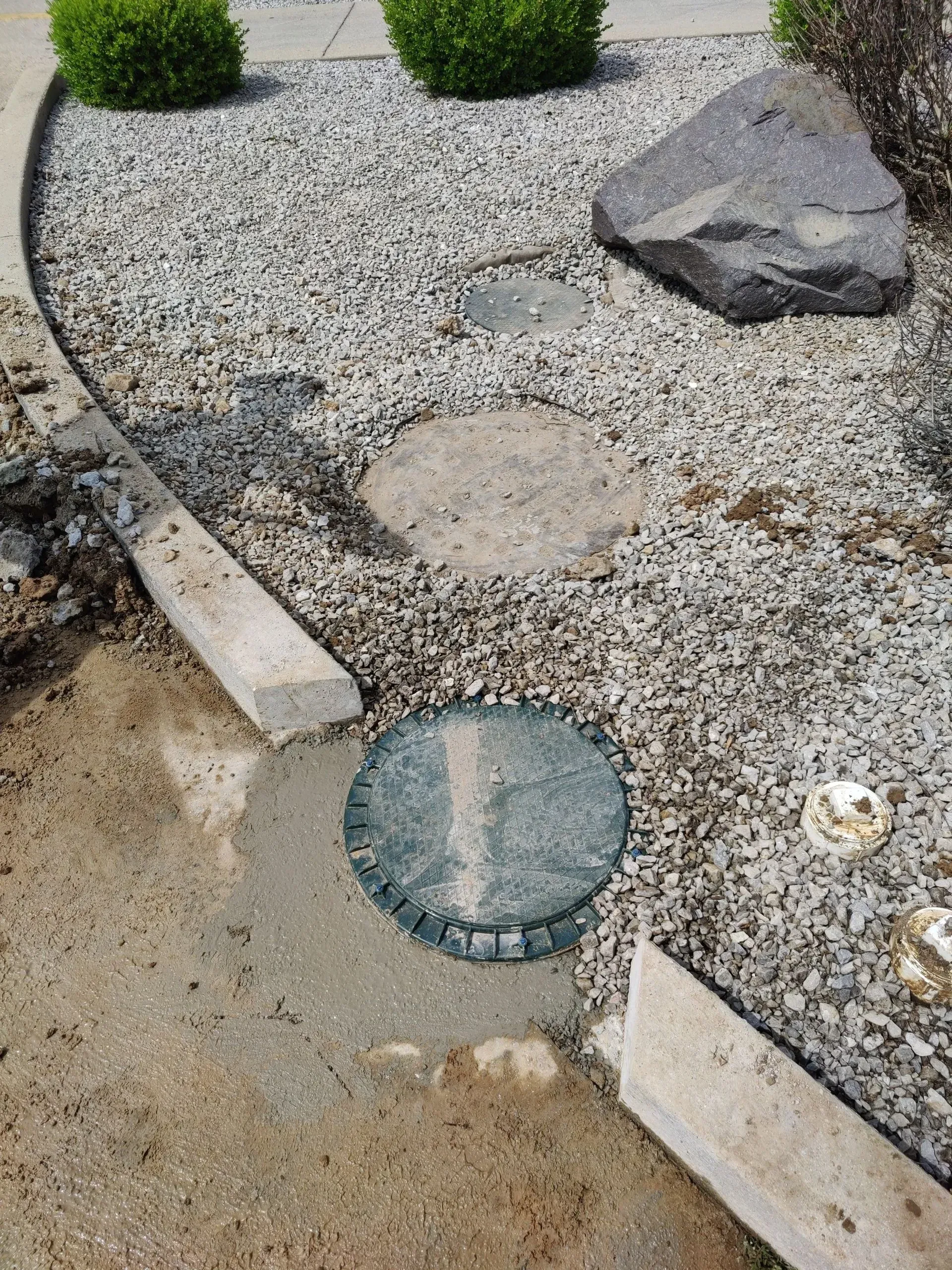 A manhole cover is sitting in the middle of a gravel path.