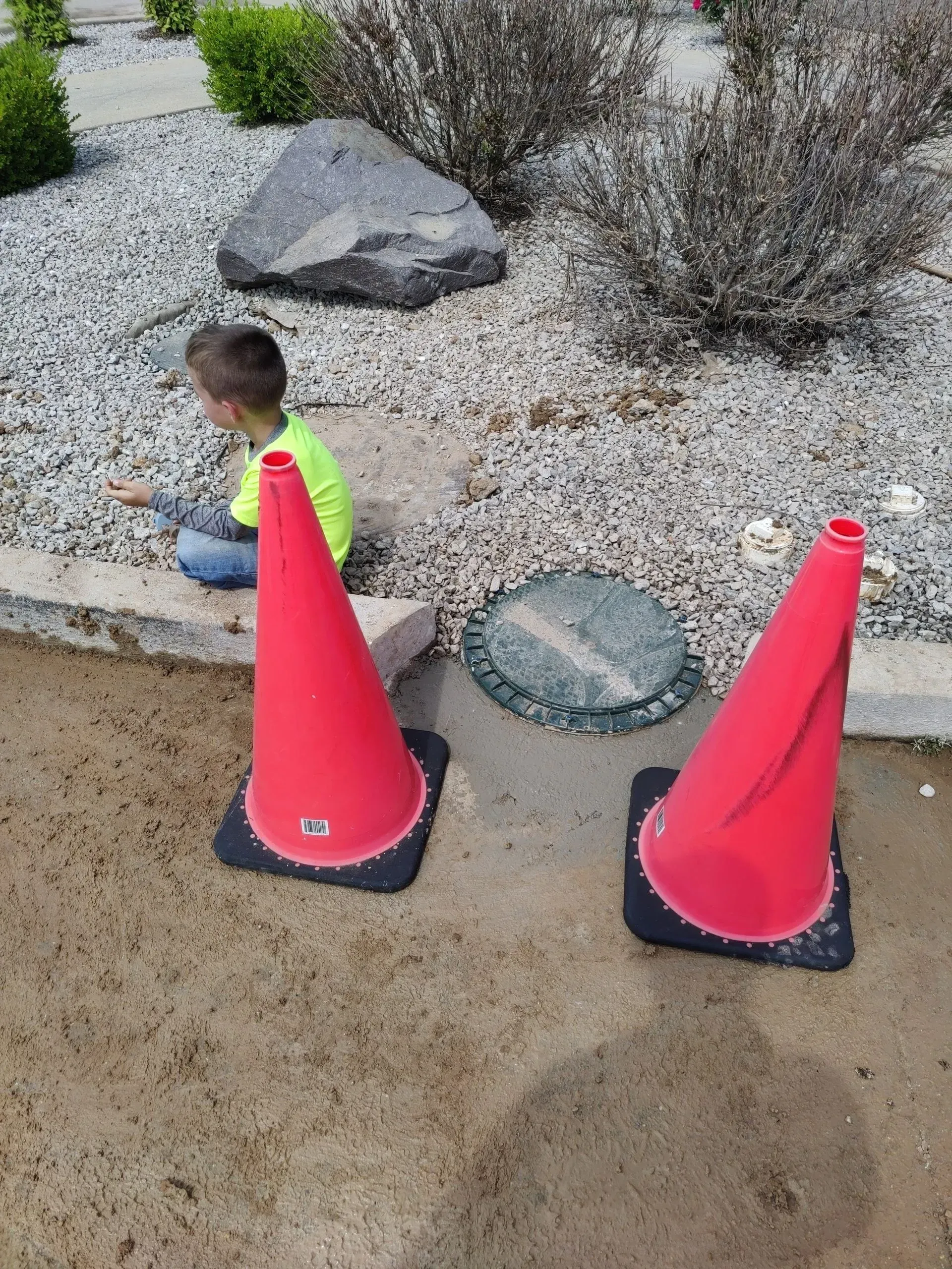 A young boy is sitting next to two red traffic cones