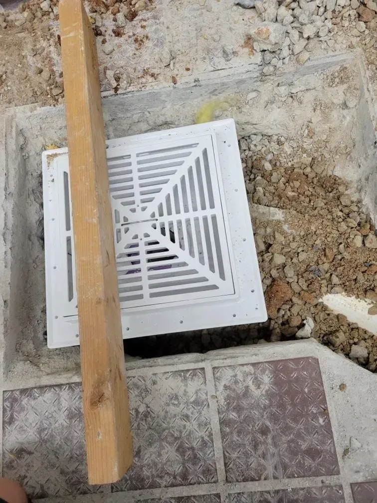 A wooden plank is sitting next to a white grille on the ground.