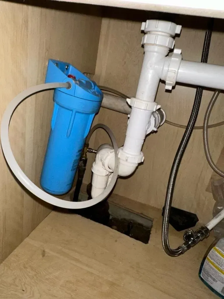 A blue water filter is attached to a white pipe under a sink.