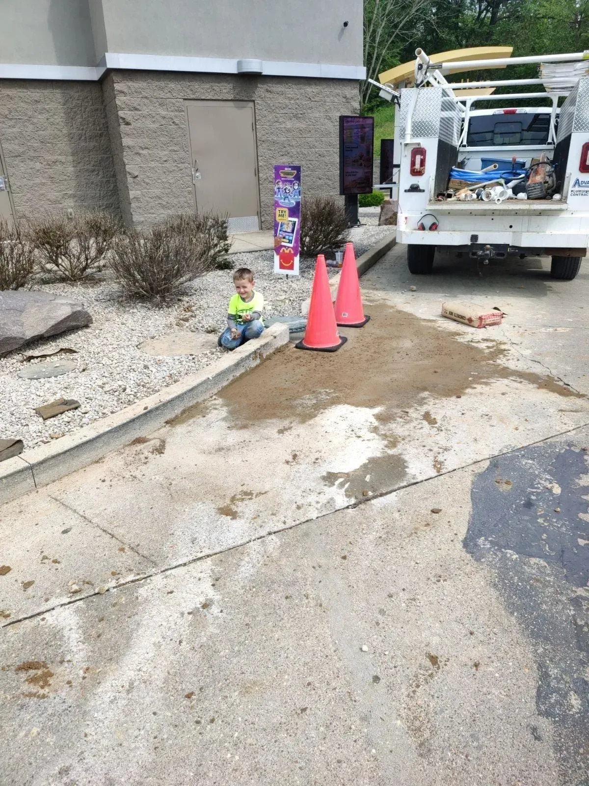 A boy is sitting on the sidewalk next to a truck and cones.