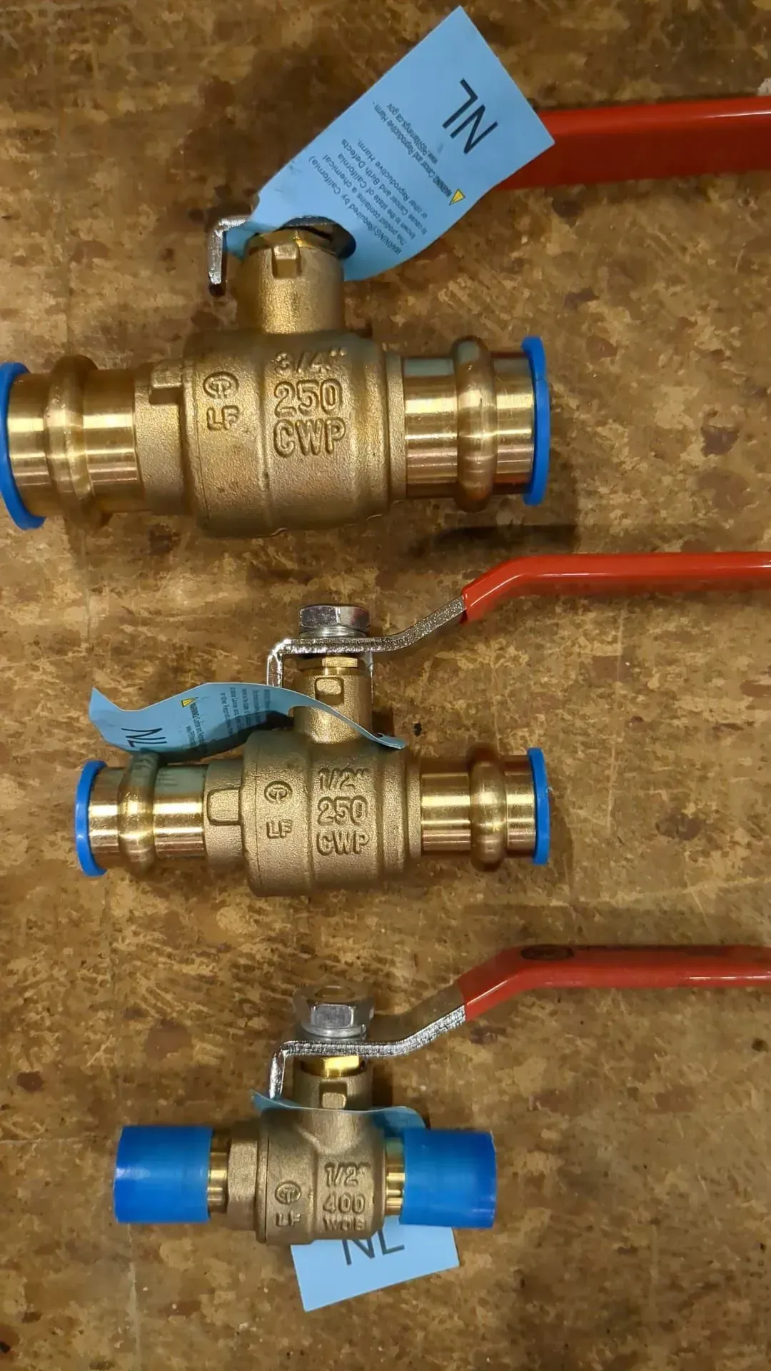 Three brass ball valves with red handles are sitting on a wooden table.