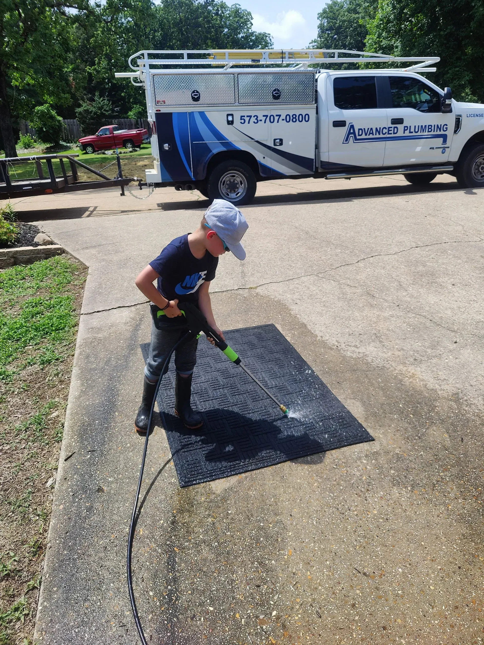 A young boy is cleaning a driveway with a high pressure washer.